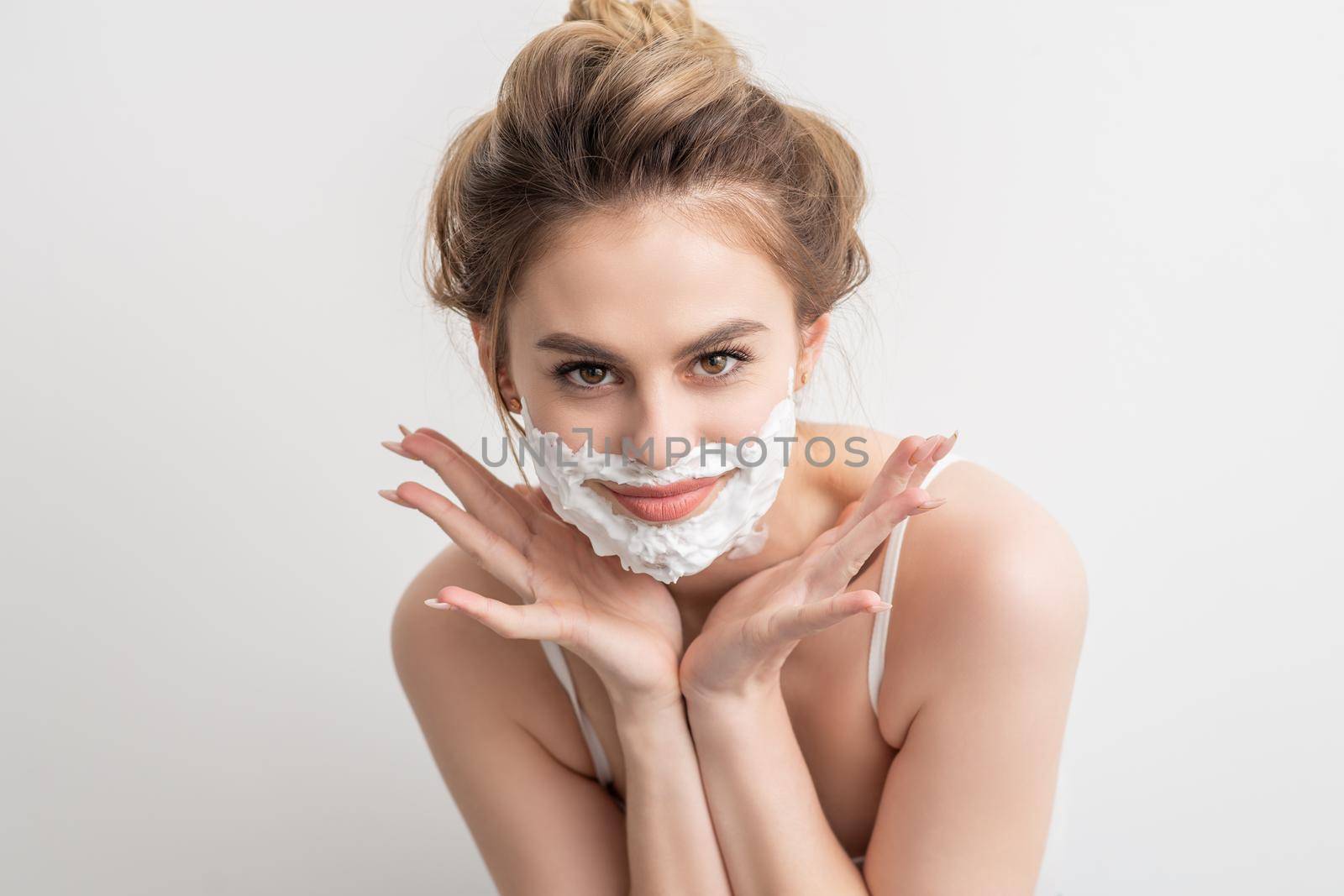 Portrait of a beautiful young smiling caucasian woman with shaving foam on face poses on white background