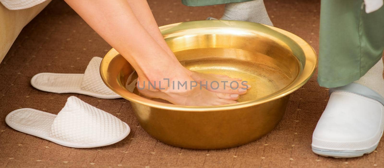 Female feet in a golden bowl with water in spa salon. Spa treatment