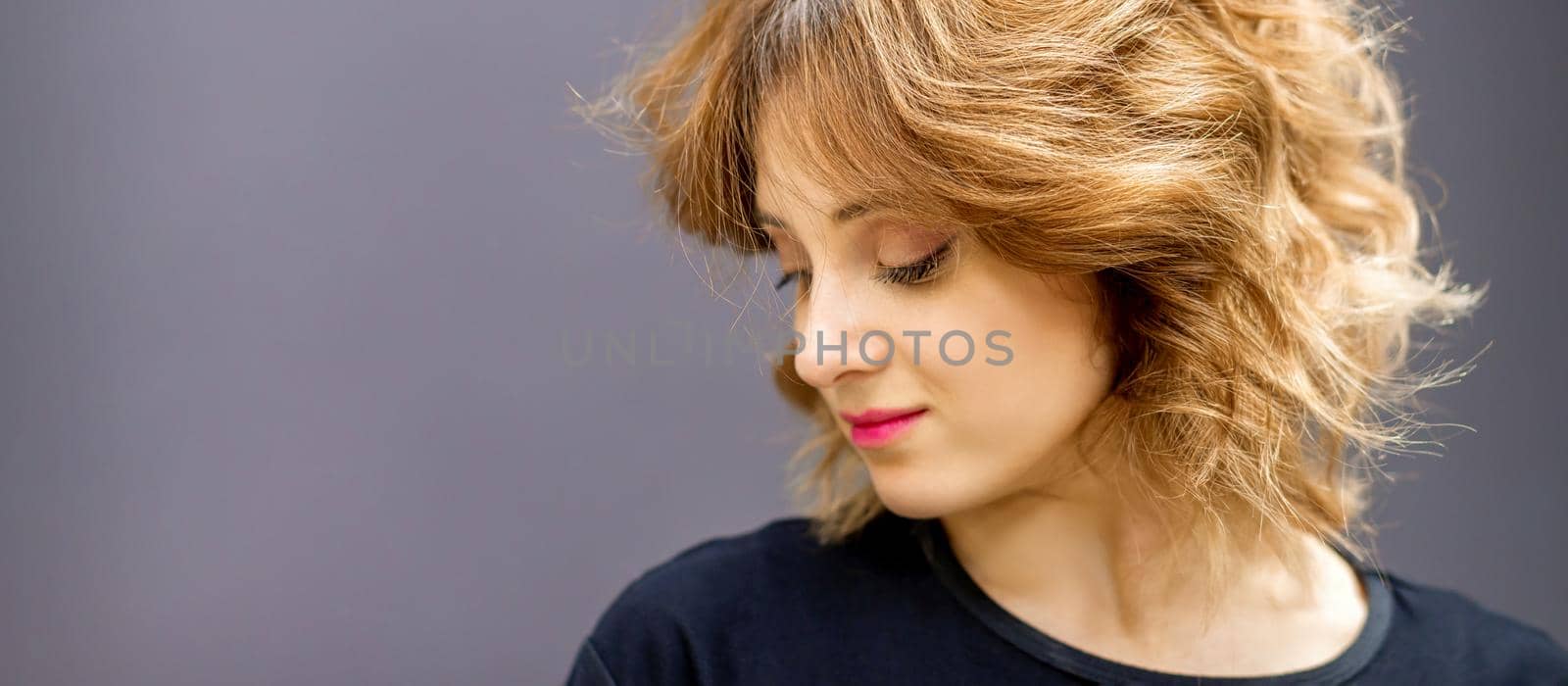 Beautiful young caucasian woman with a red short curly hairstyle looking down on dark background