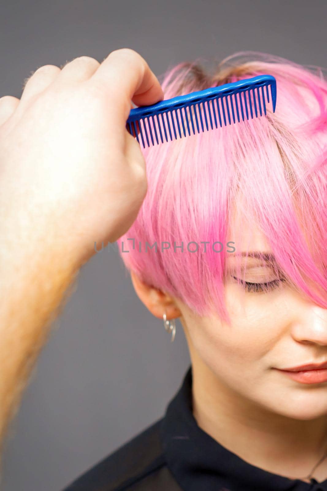 Professional hairdresser checks hairstyle with a comb of young beautiful caucasian woman