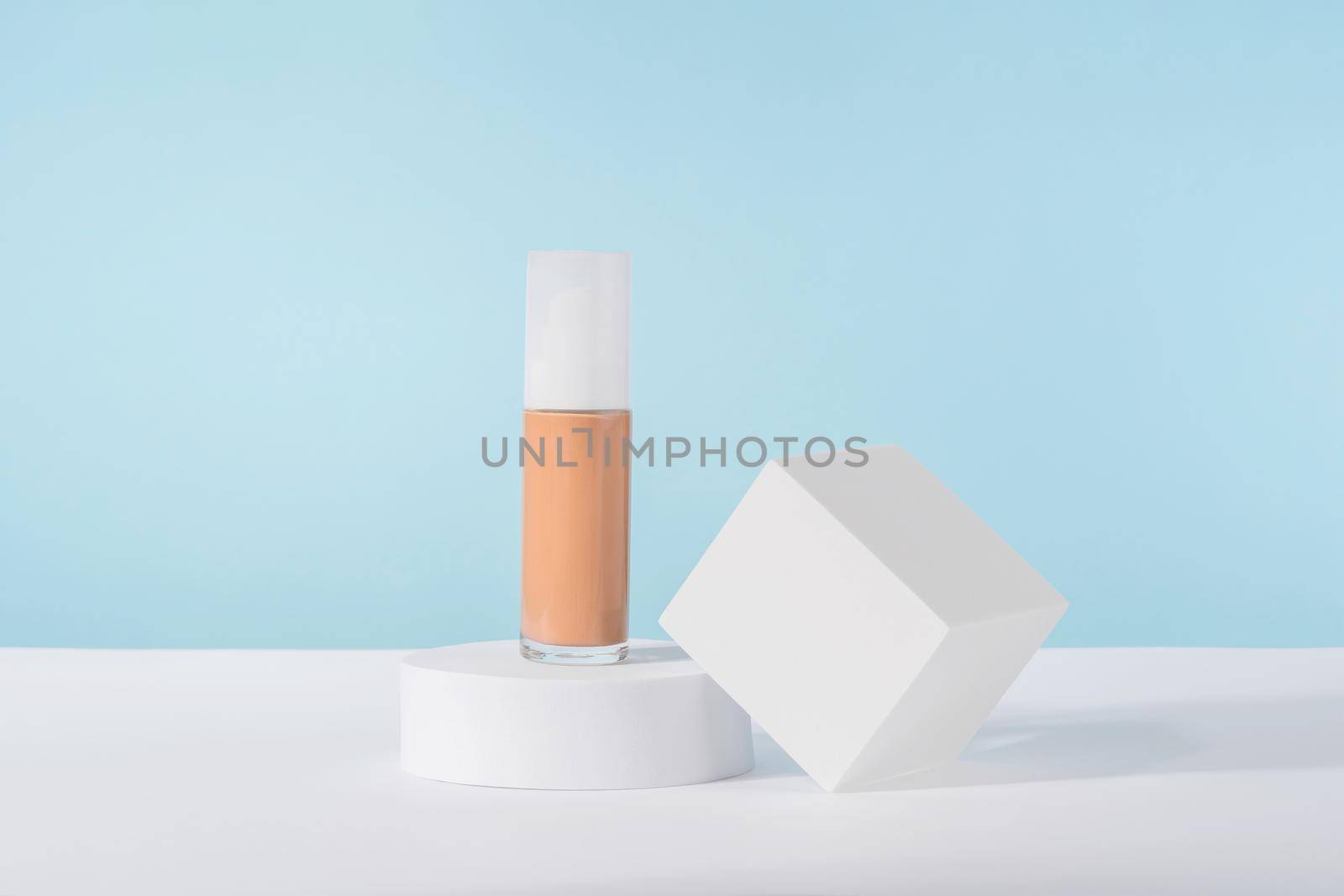 Cosmetic liquid foundation nude cream bottle mockup on white square block podium pedestal. Beige concealer base cosmetics product mock up on blue backdrop. Skincare beauty primer, bb corrector