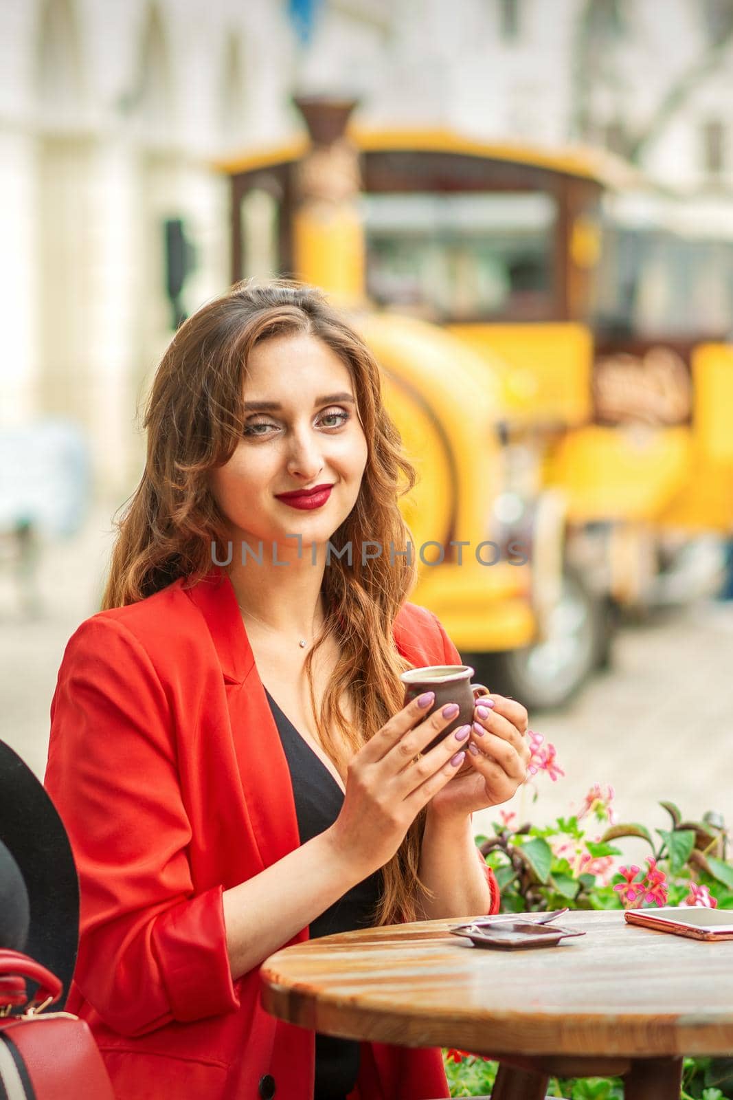 Tourist young caucasian woman in red jacket with coffee cup at the table in cafe outdoors