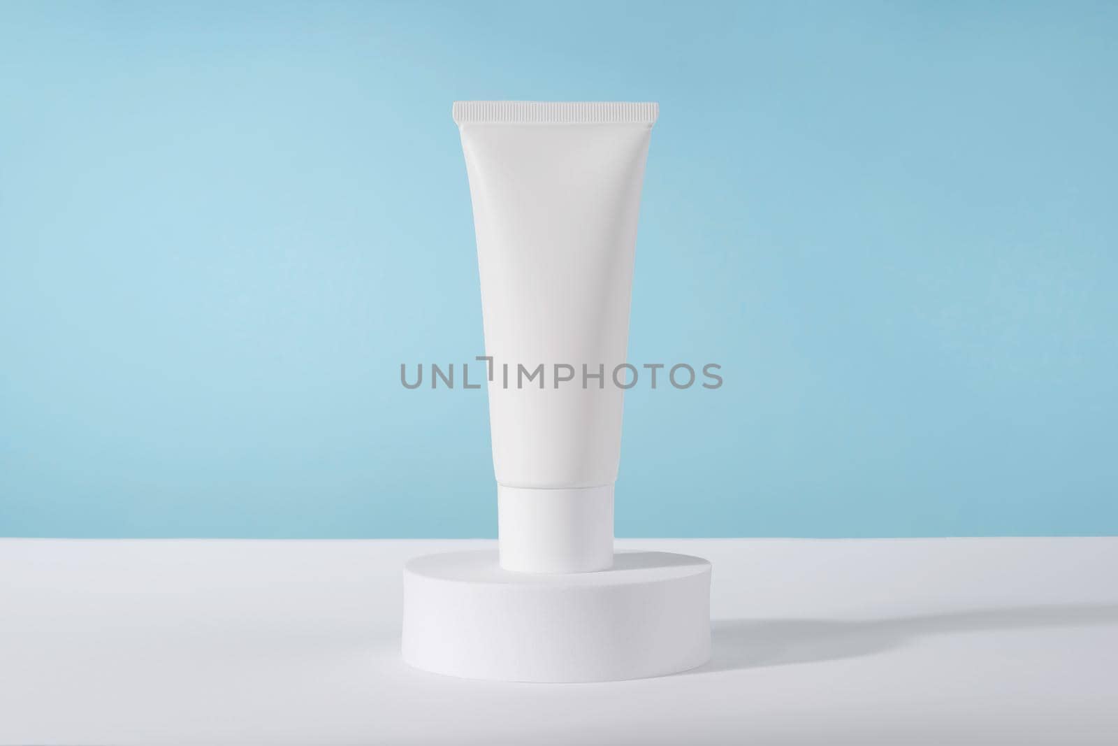 Cosmetic luxury cream tube bottle mockup on blue background on pedestal podium. Unbranded lotion beauty product packaging. Product presentation . Lotion, mousse, cleanser for skincare routine by photolime