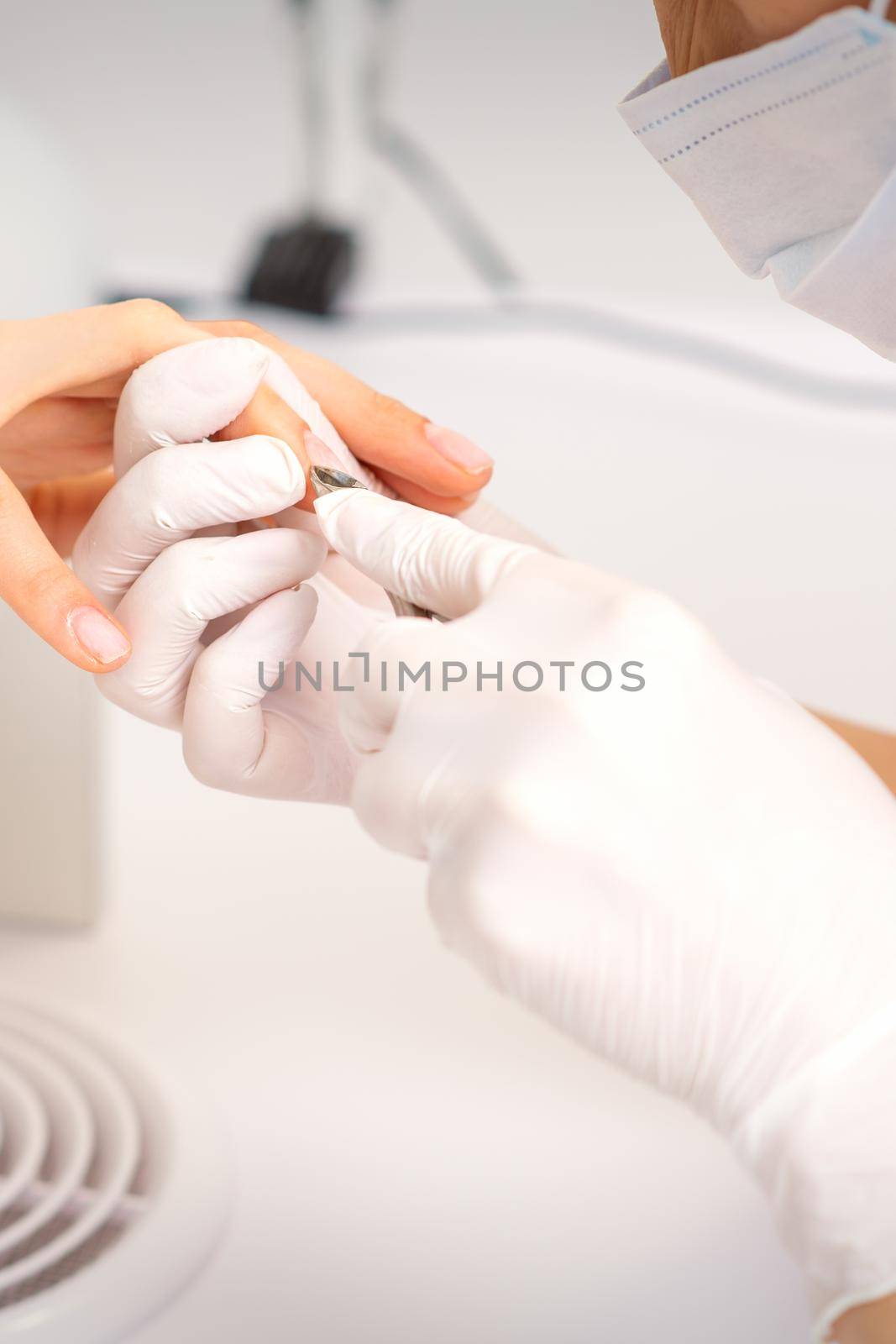 Close up of manicure master with manicure nipper cuts cuticles of female nails at beauty salon