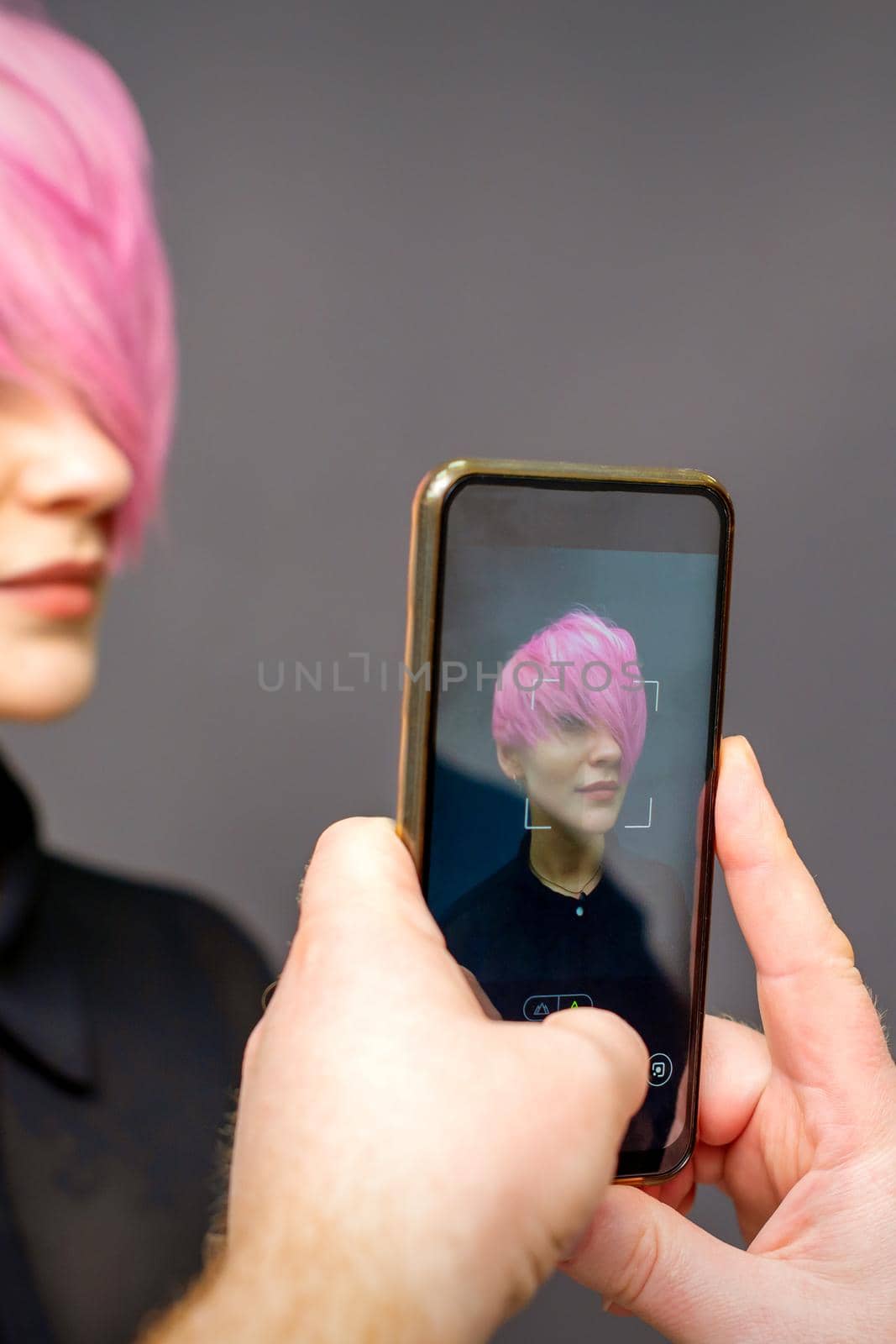 Man hairdresser's hands taking picture on smartphone of her client short pink hairstyle