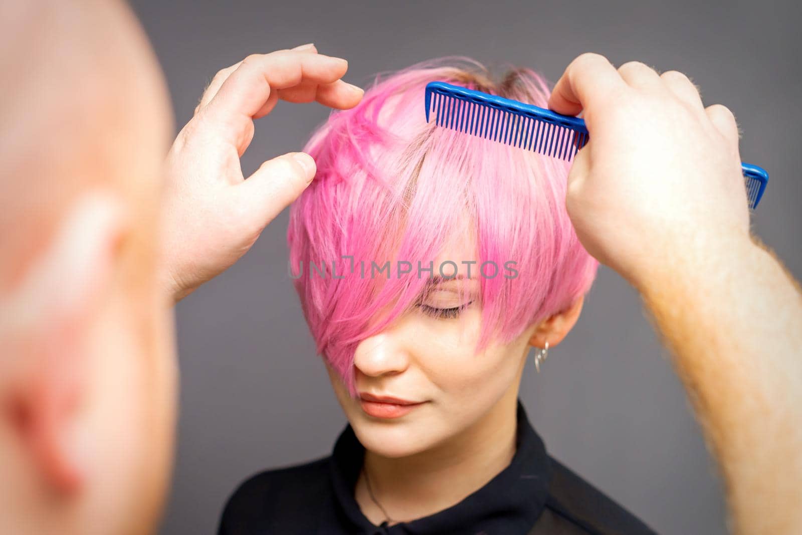 Professional hairdresser checks hairstyle with a comb of young beautiful caucasian woman