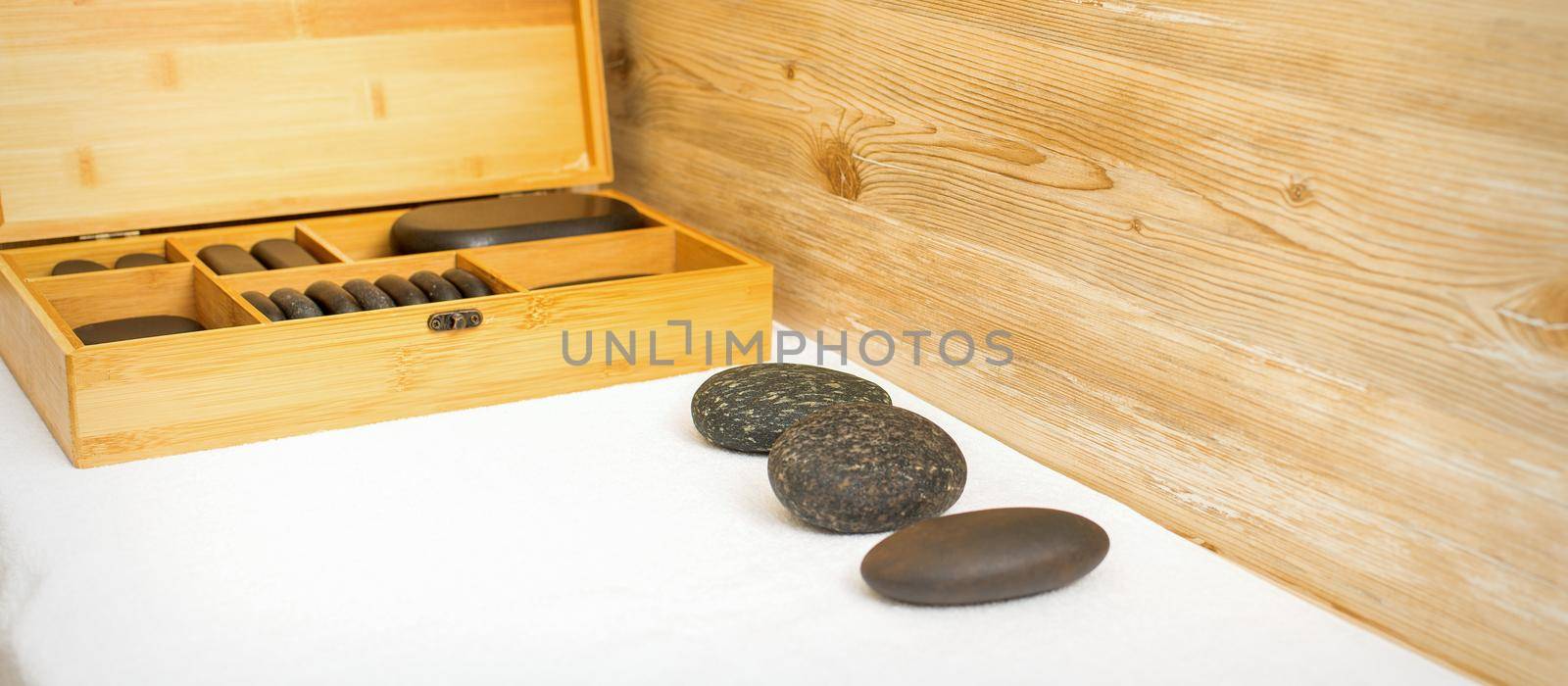 Black massage stones lying near the wooden box with massage rocks on the towel on the table