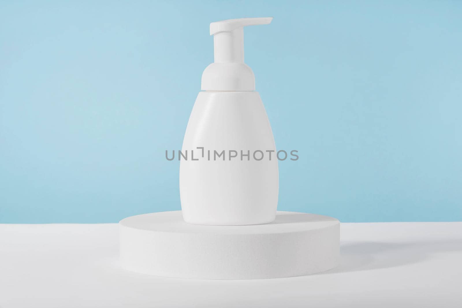 Bath soap white cosmetic bottle mockup on white podium pedestal on blue background. Body care foam product or lotion packaging. Plastic cosmetics tube front view mock up. Body hygiene cream