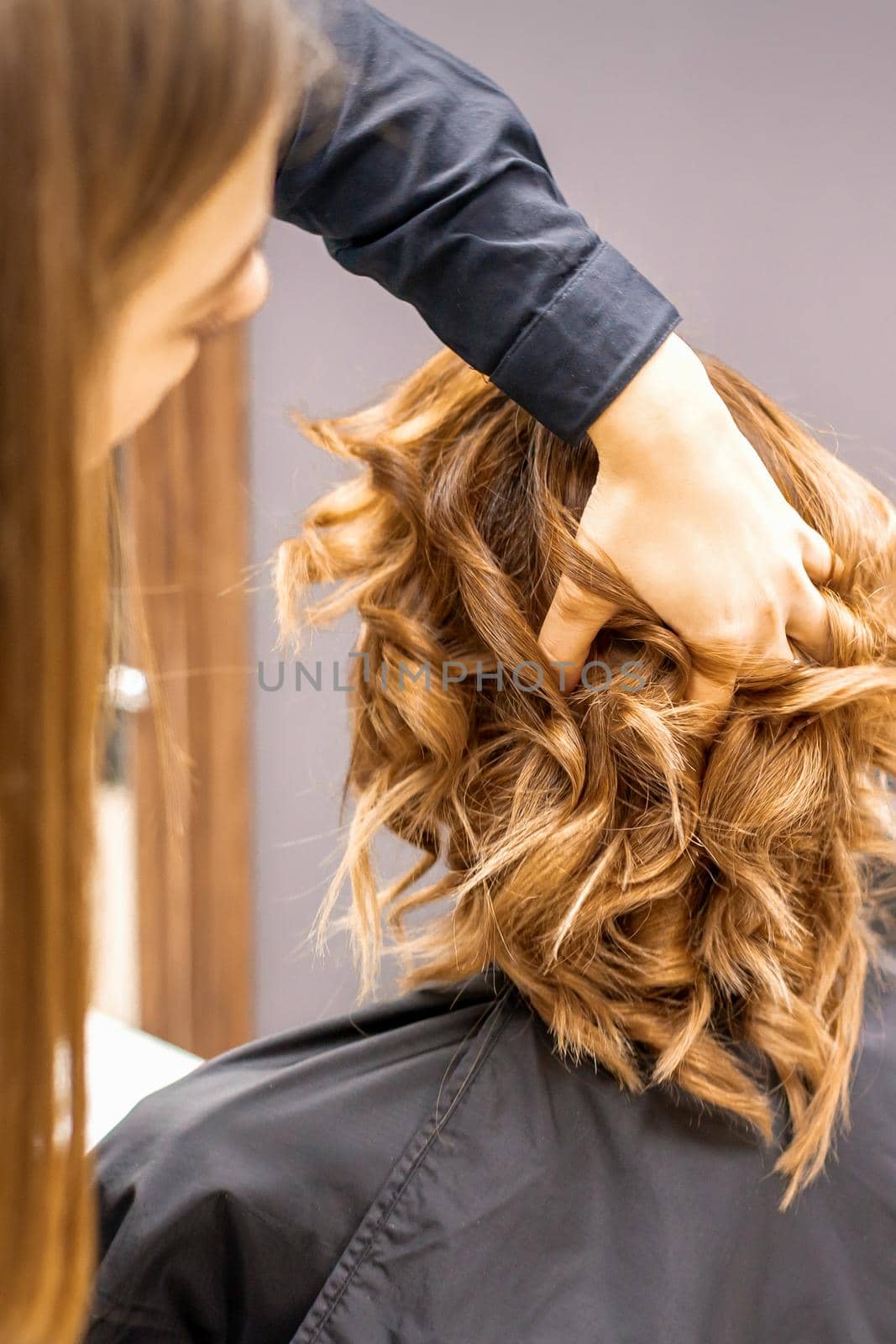 Female hairdresser checks brown curly hairstyle of a young caucasian woman in beauty salon