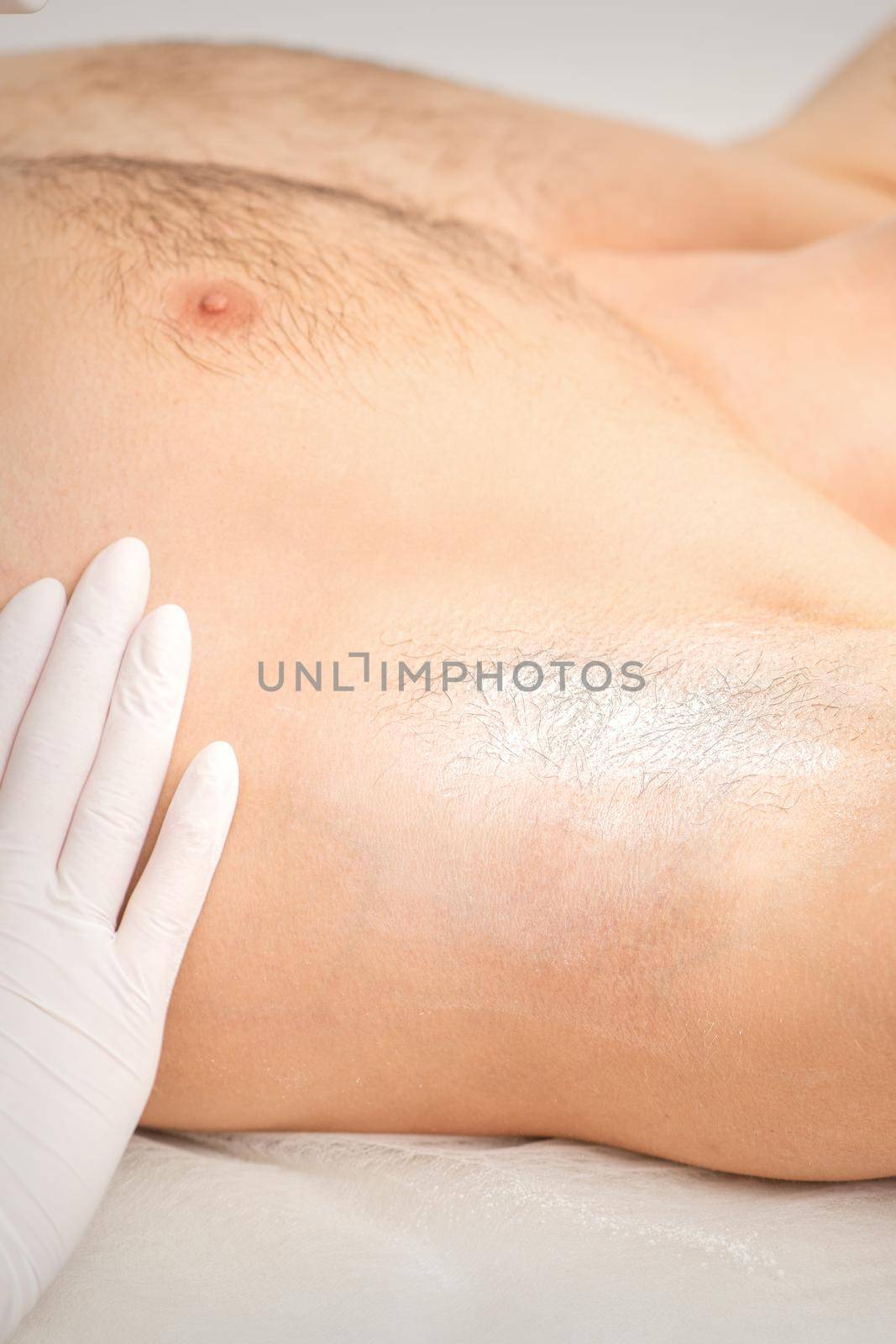 Young caucasian man receiving hair removal from his armpit in a beauty salon, depilation men's underarm