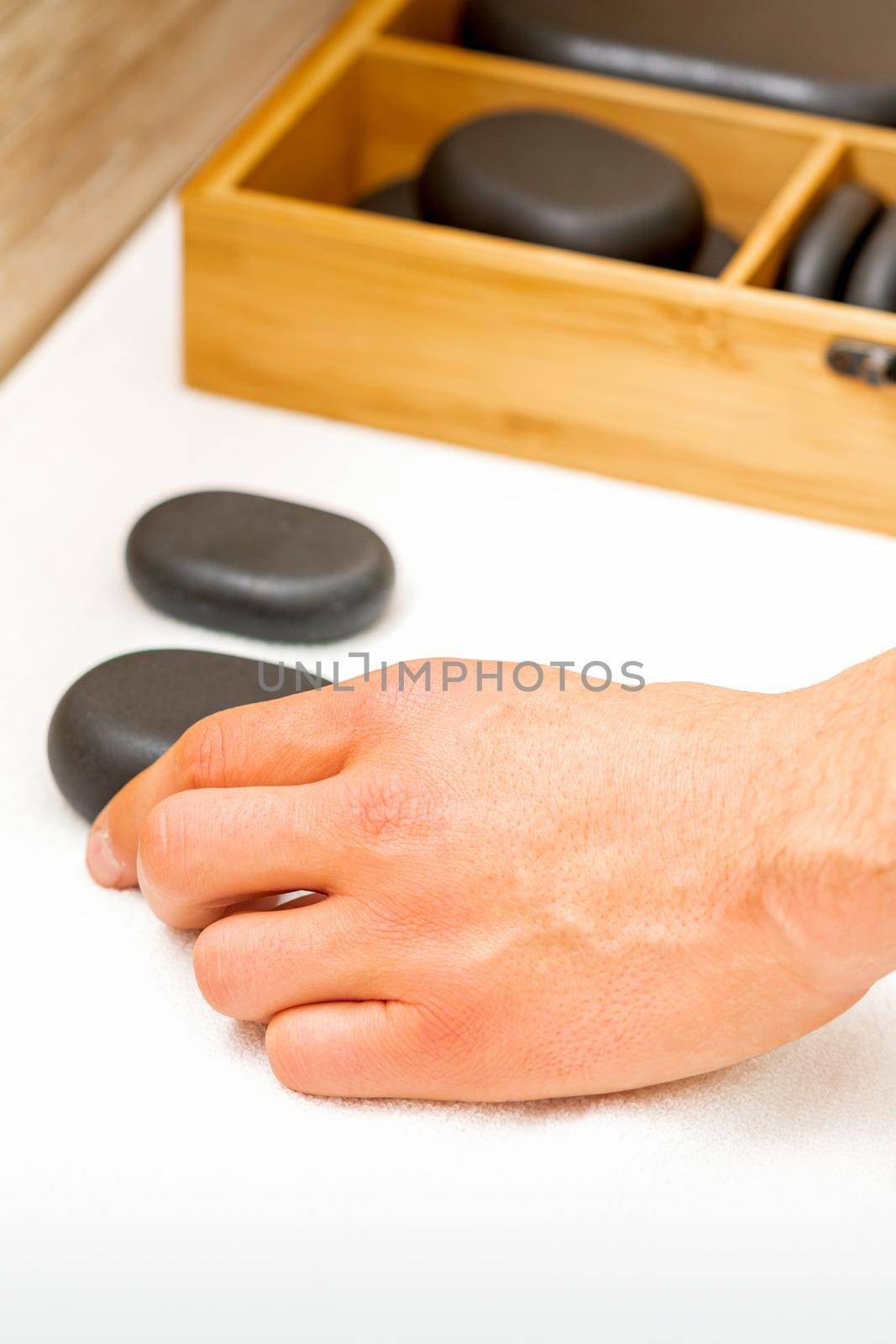 Hand of masseur takes black massage stones from the table in spa salon