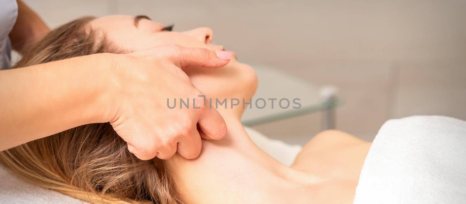Beautician making lymphatic drainage face massage or facelifting massage at the beauty salon. by okskukuruza