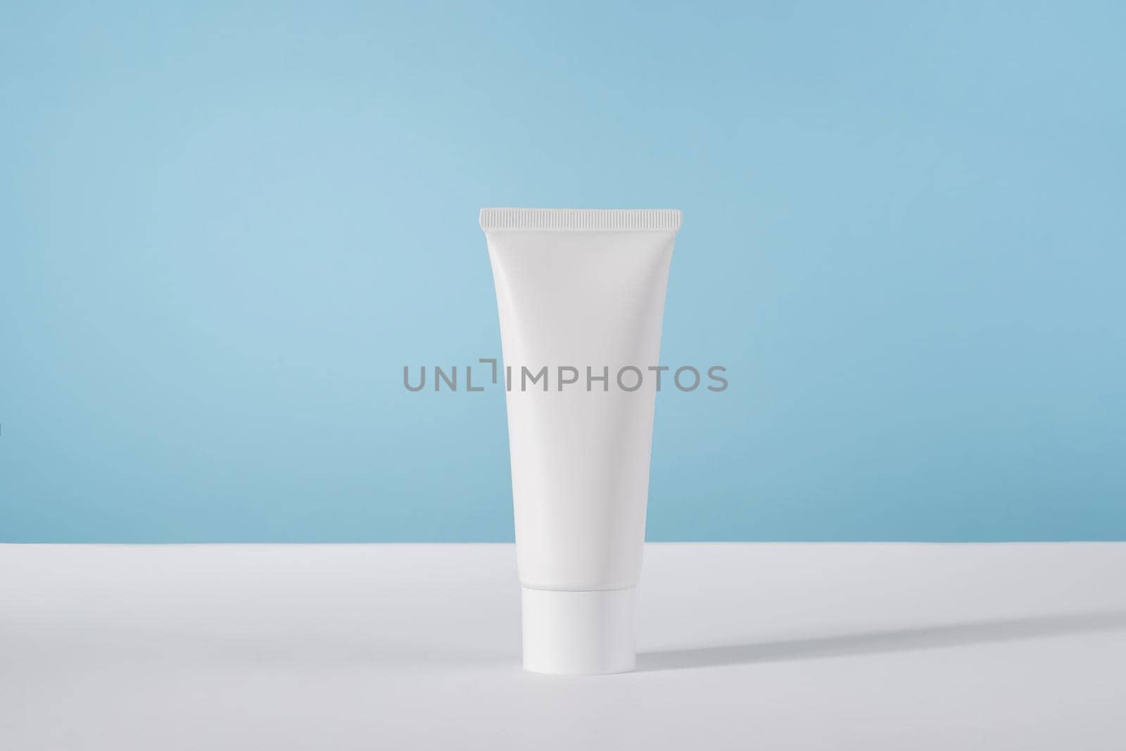 Moisturiser hand cosmetic cream white plastic tube mockup on blue background front view. Blank body and health care beauty product packaging by photolime
