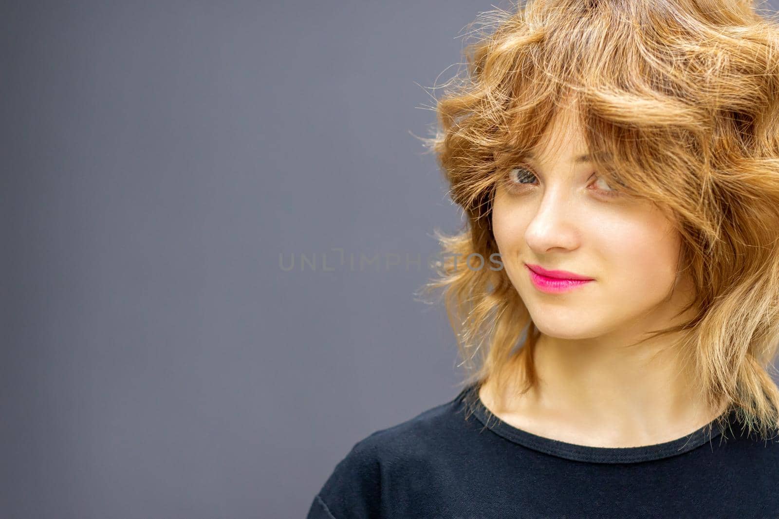 Beautiful young caucasian woman with a red short curly hairstyle on dark background