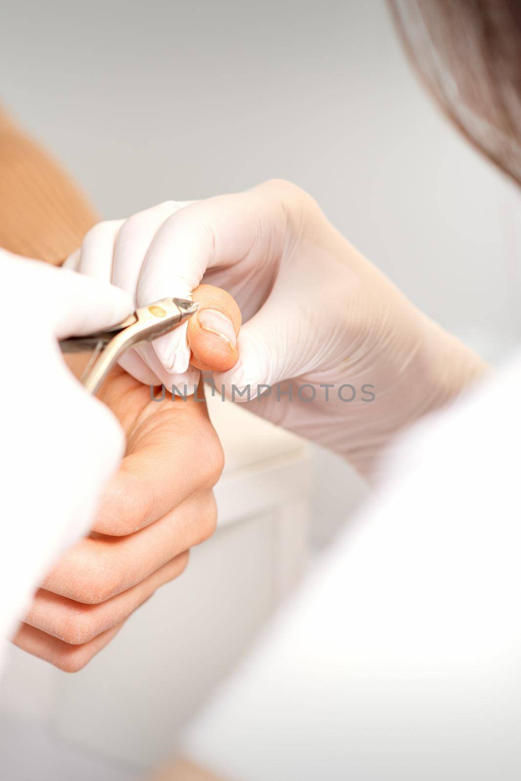 Close up of manicure master with manicure nipper cuts cuticles of female nails at beauty salon