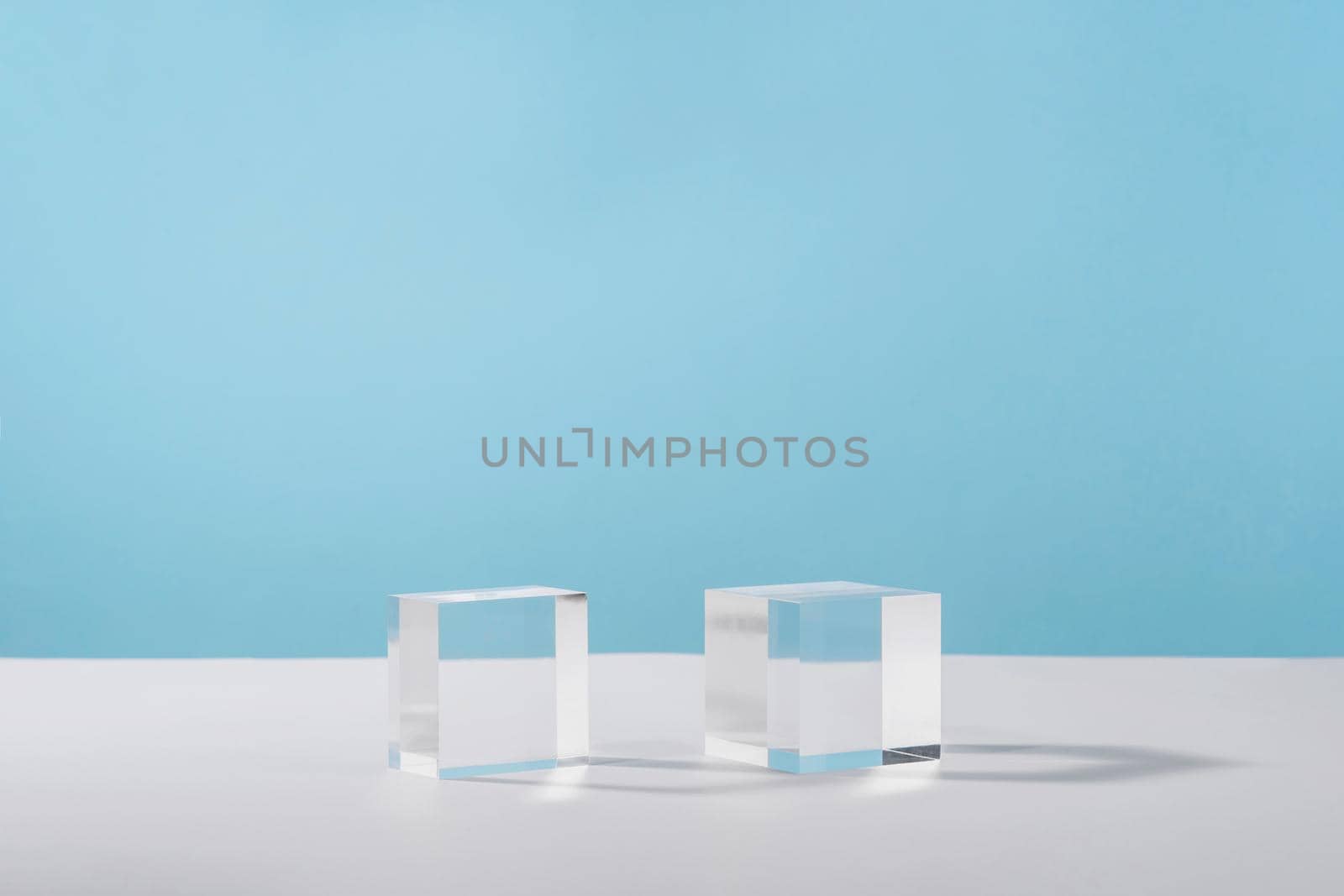 Pedestal cosmetic display glass podium platform with stylish props for product presentation, cosmetics geometric stand, mockup scene for jewellery. Acrylic blocks cubeson blue background