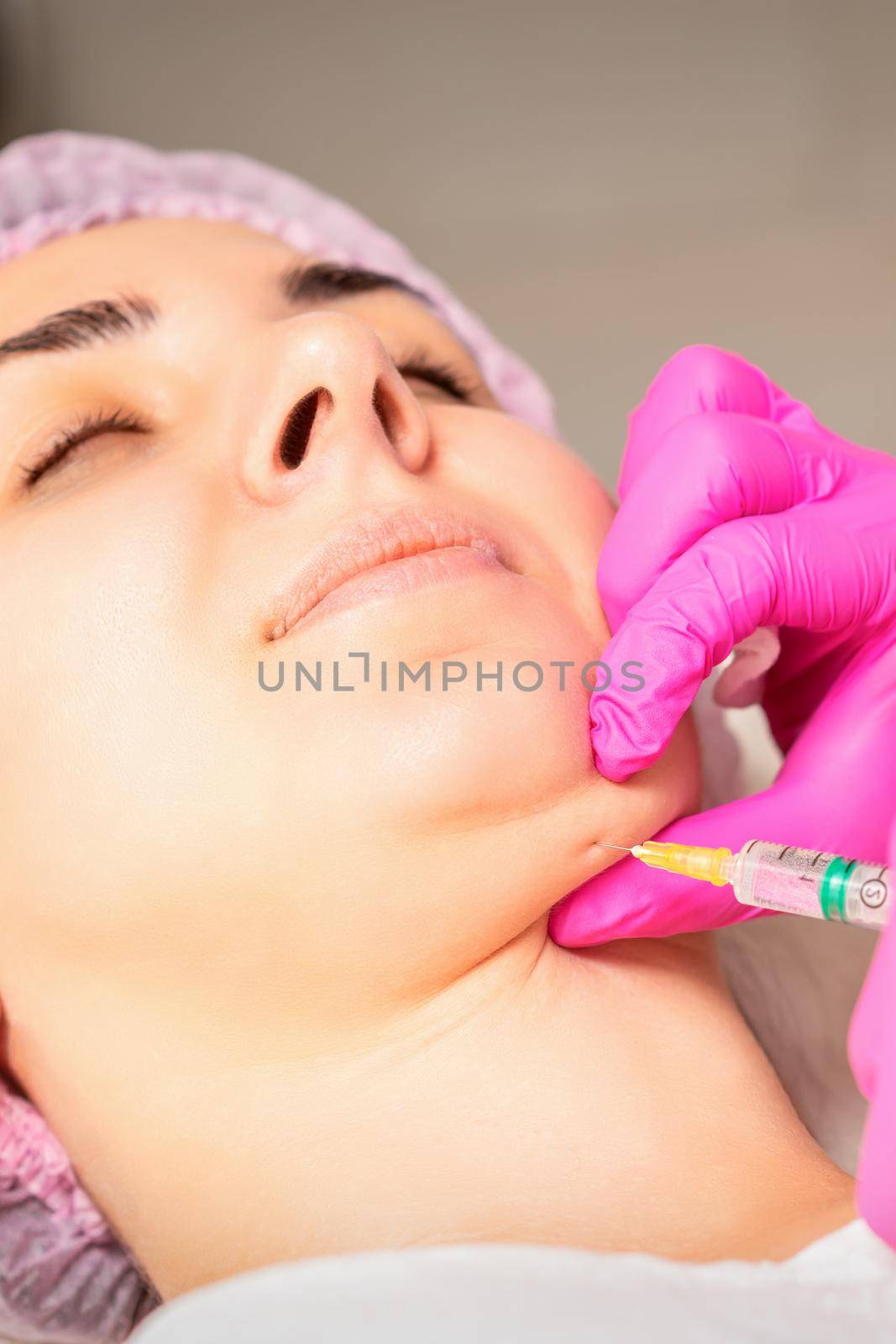 The cosmetologist makes lipolytic injection on the chin of a young woman against the double chin in a beauty salon