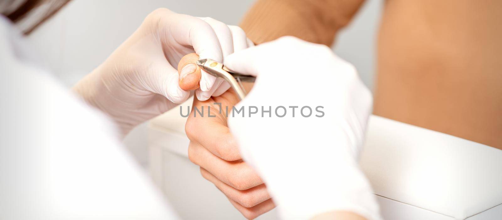 Close up of manicure master with manicure nipper cuts cuticles of female nails at beauty salon