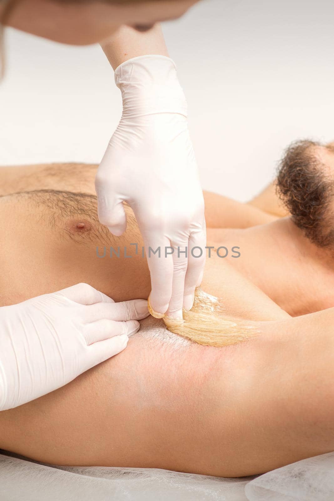 Young caucasian man receiving hair removal from his armpit in a beauty salon, depilation men's underarm