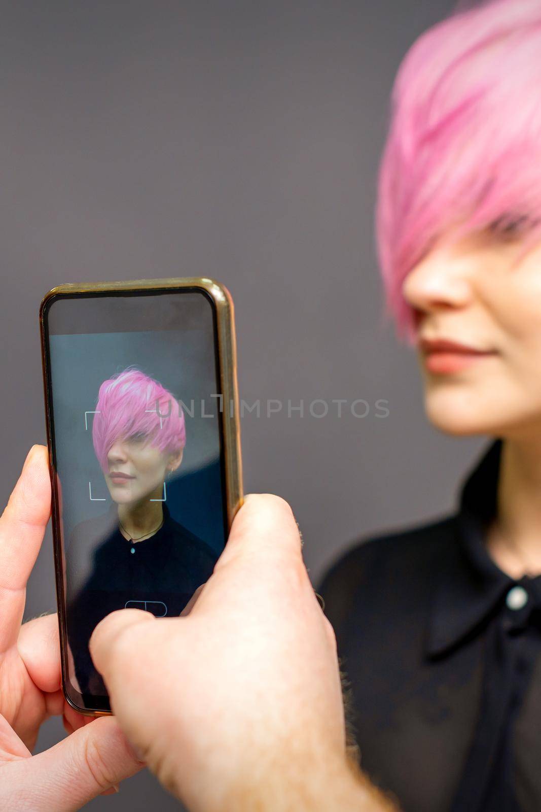 Man hairdresser's hands taking picture on smartphone of her client short pink hairstyle