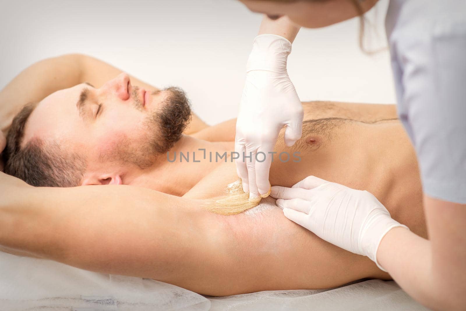 Young caucasian man receiving hair removal from his armpit in a beauty salon, depilation men's underarm