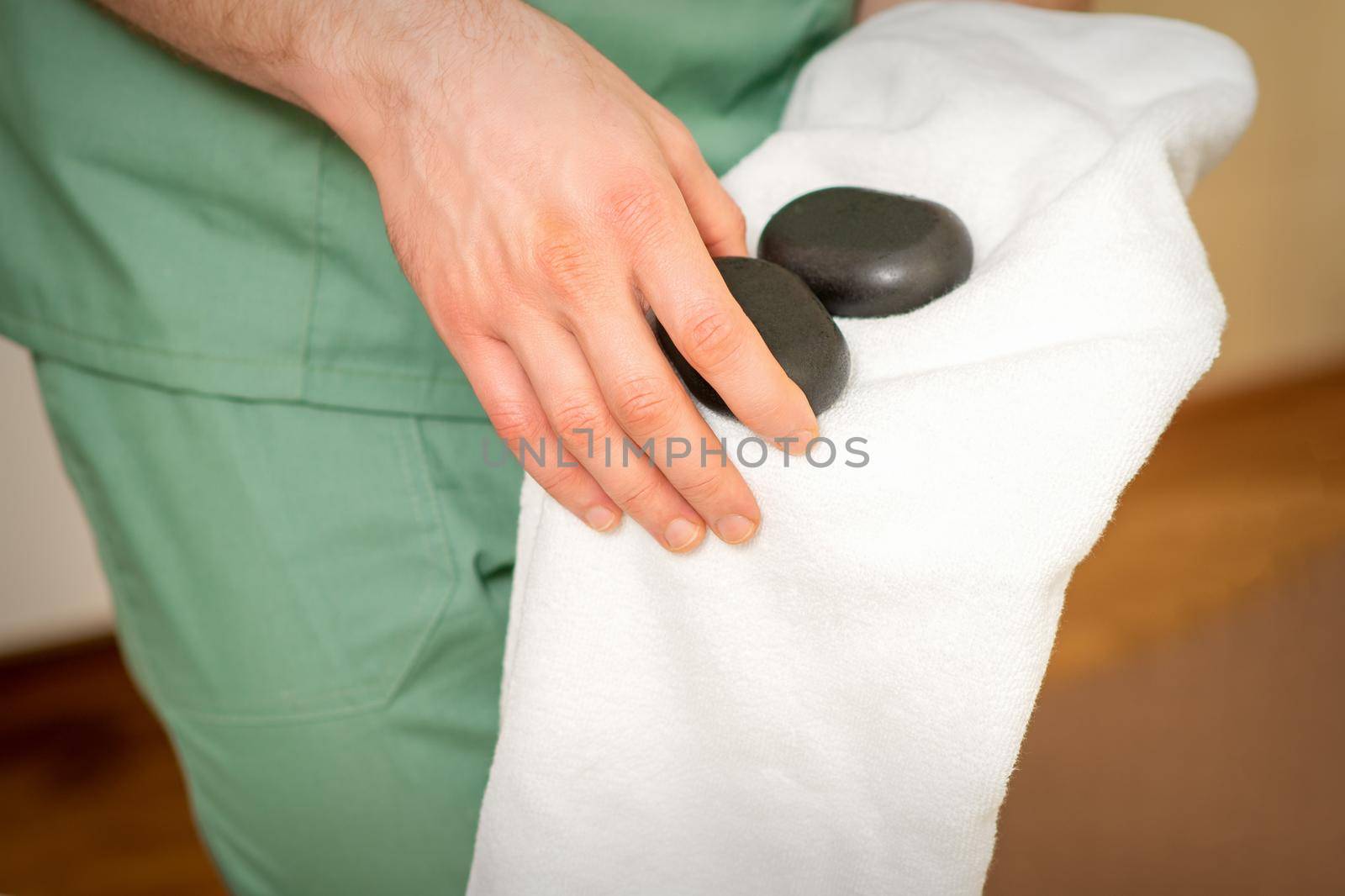 Close up of masseur's hand wipes black massage stones with a white towel