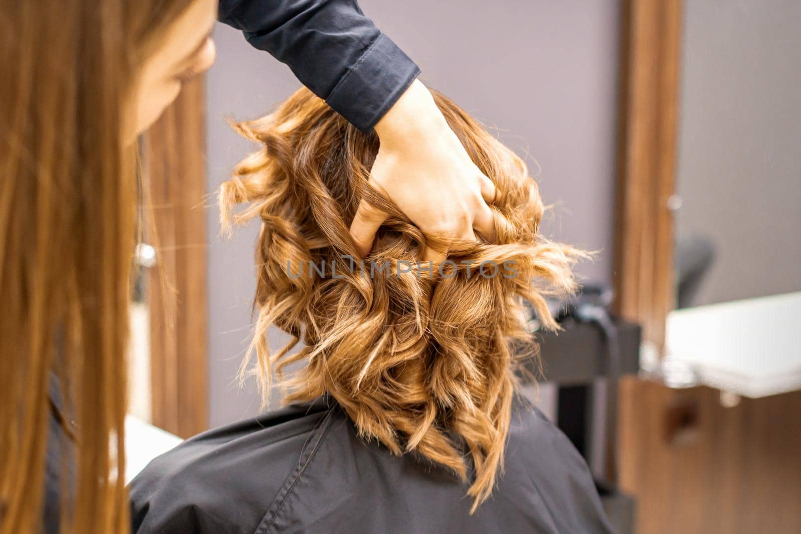 Female hairdresser checks brown curly hairstyle of a young caucasian woman in beauty salon