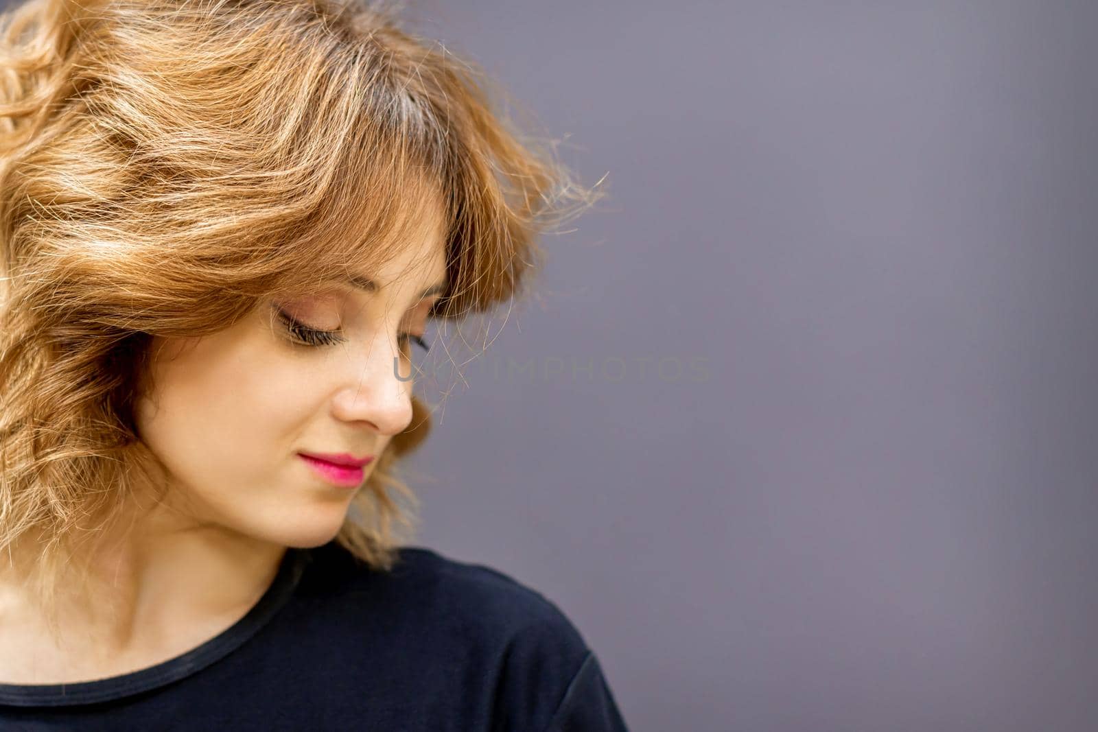 Beautiful young caucasian woman with a red short curly hairstyle looking down on dark background