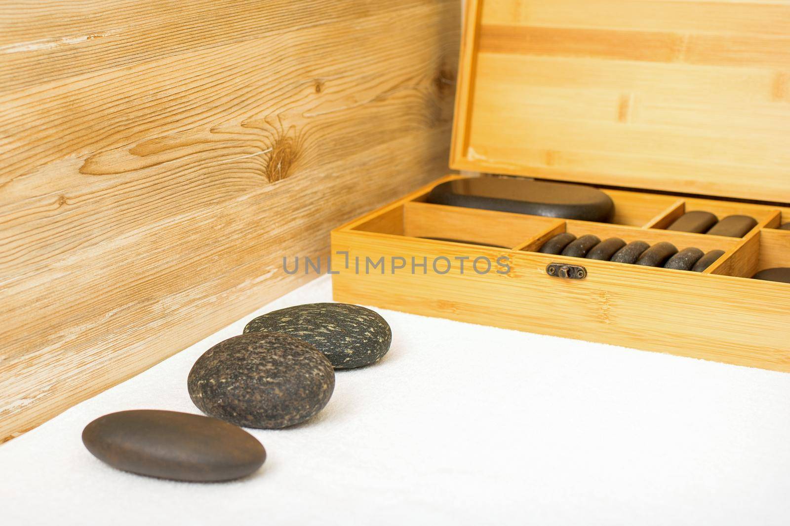 Black massage stones lying near the wooden box with massage rocks on the towel on the table
