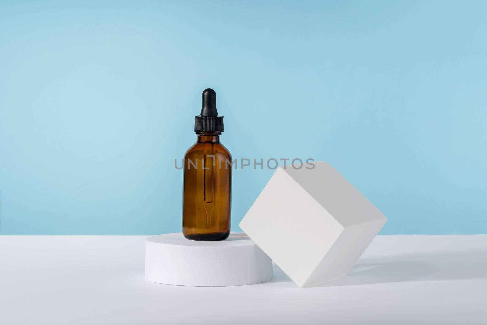 Oil cosmetics amber product packaging with stylish props. Serum cosmetic bottle with peptides and retinol on platform pedestal on blue background. Serum dropper mockup