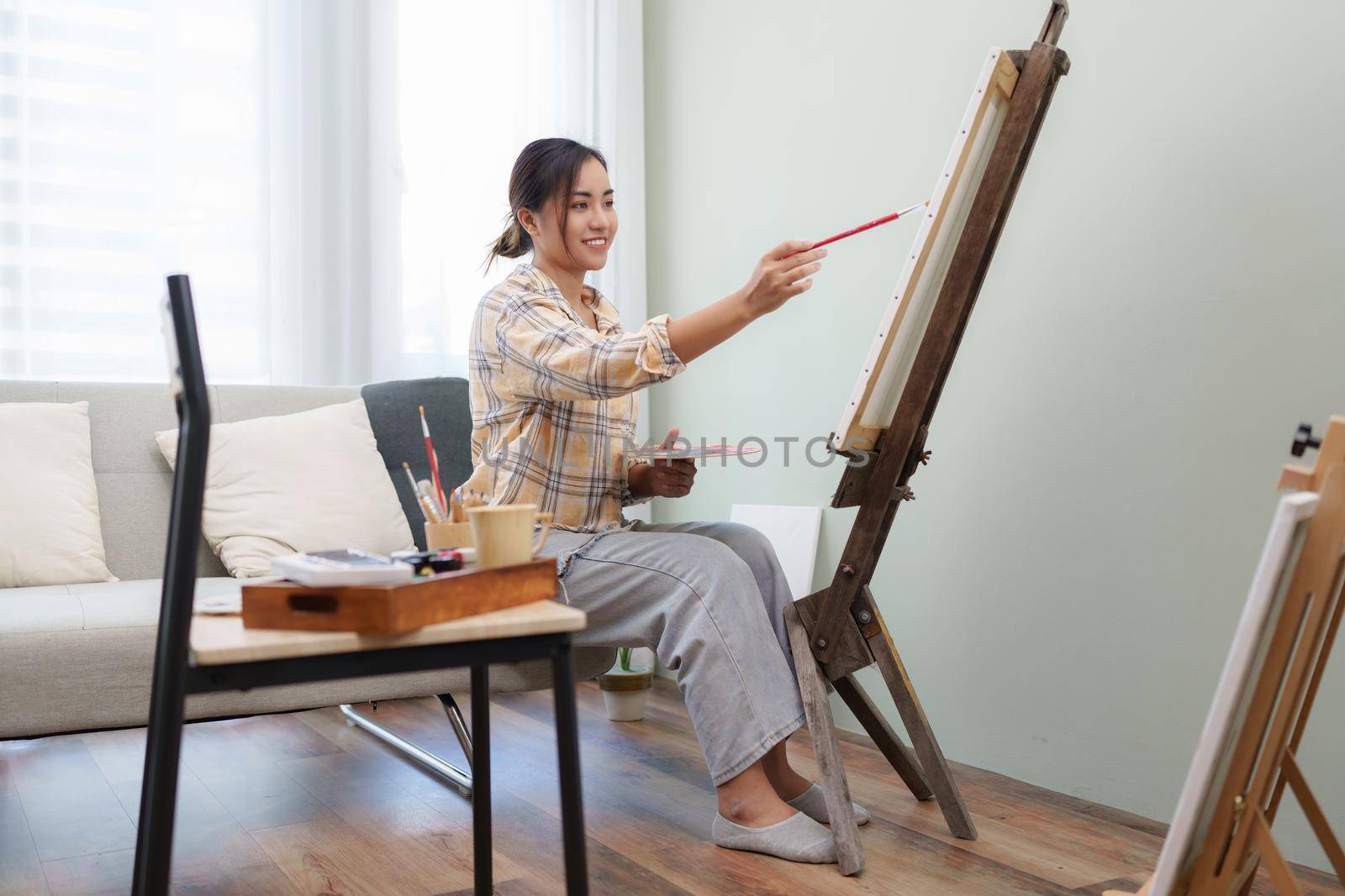 Joyful young female artist painting on canvas at workshop.