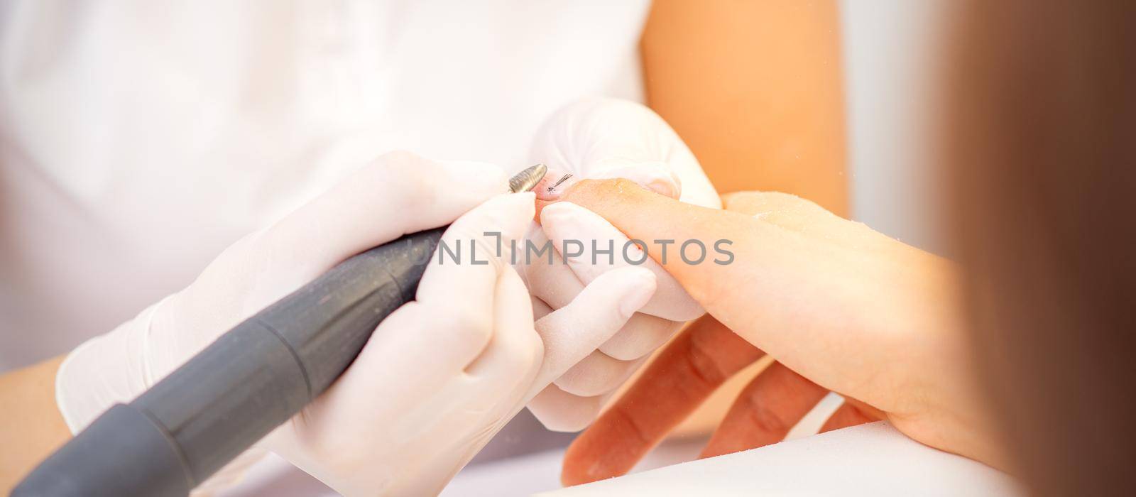 Closeup of manicure master in white gloves applying an electric nail file drill to remove the nail polish in the beauty salon