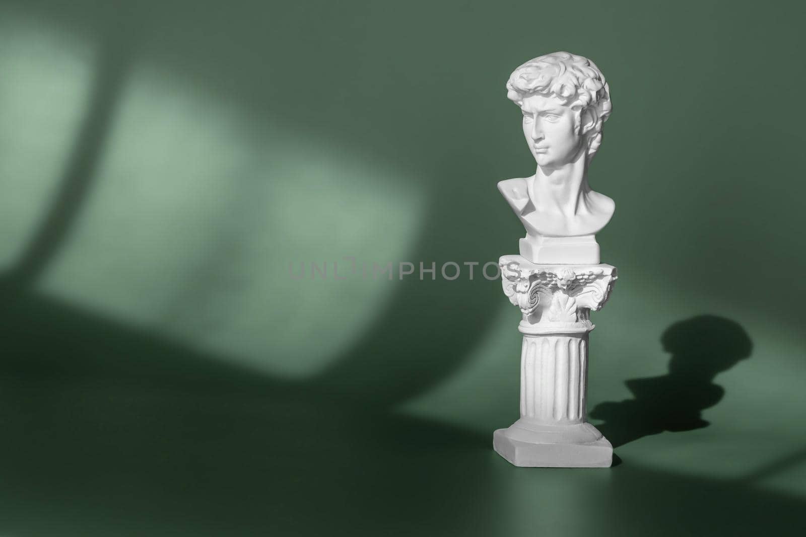White marble head of young man, head of famous statue by Michelangelo - David from Florence. Gypsum copy of ancient statue head on green background with light and shadow