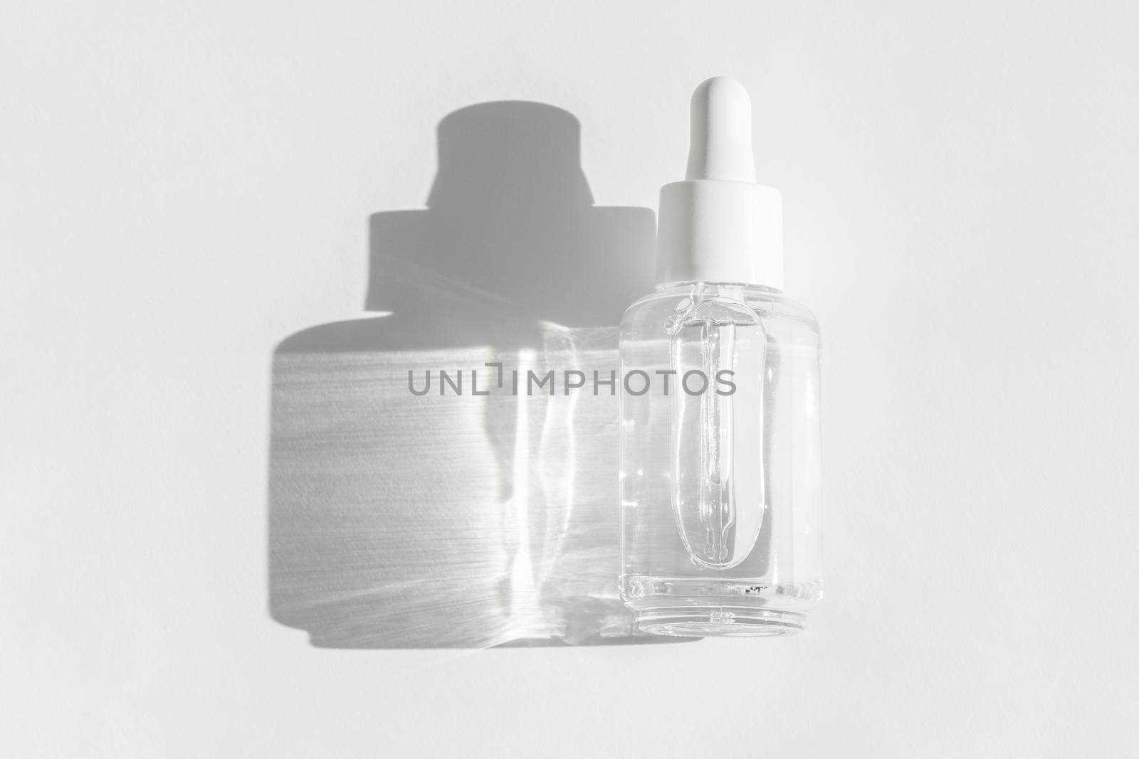 Anti aging serum with collagen and peptides on white with sunlight and shadow. Hyaluronic or polyglutamic acid oil cosmetic mockup. Transparent liquid product packaging in glass bottle. by photolime