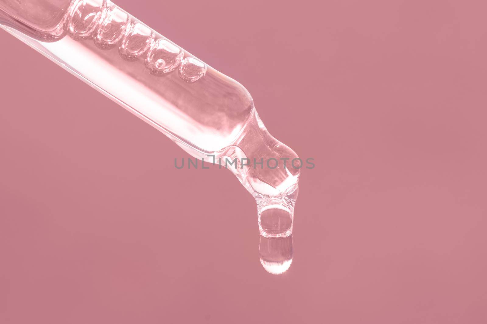 Closeup of pink dropper, falling drop close up. Beauty skin care product. Pipette with essential oil, serum with peptides, hyaluronic acid on pink background. Self care by photolime