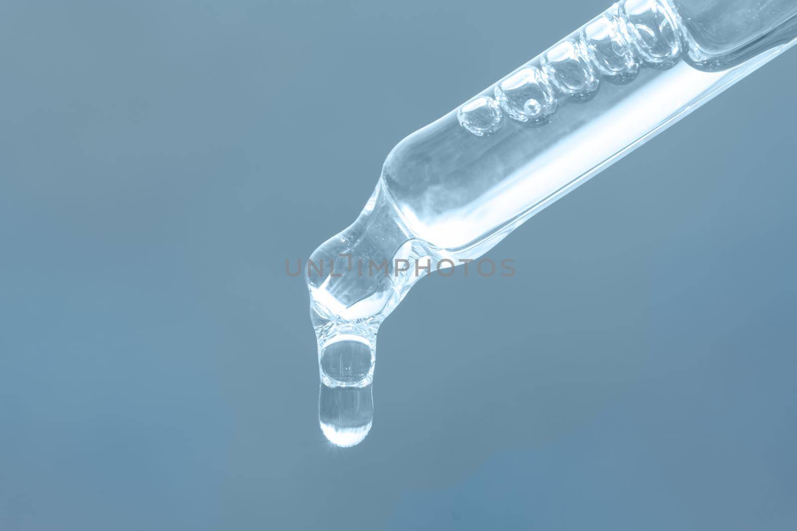Beauty skin care product. Pipette with essential oil, serum with peptides, hyaluronic acid on blue background. Closeup of blue dropper, falling drop close up. Self care concept