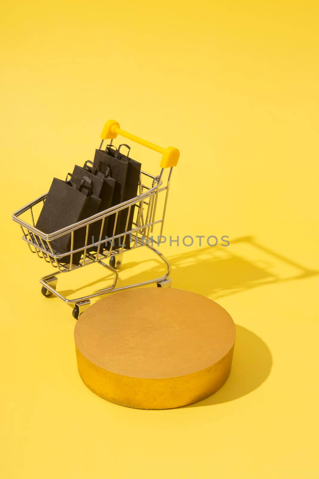 Empty mockup podium or pedestal and miniature supermarket cart with shopping bags in black friday sale on yellow