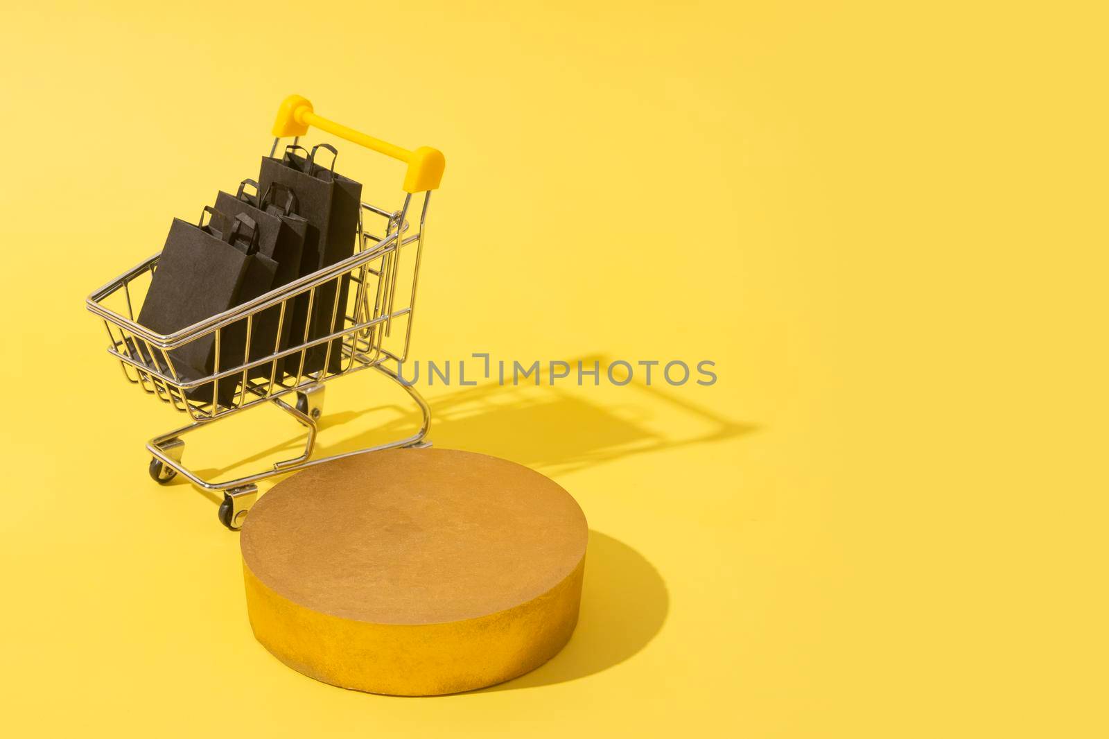 Empty mockup podium or pedestal and miniature supermarket cart with shopping bags in black friday sale on yellow.