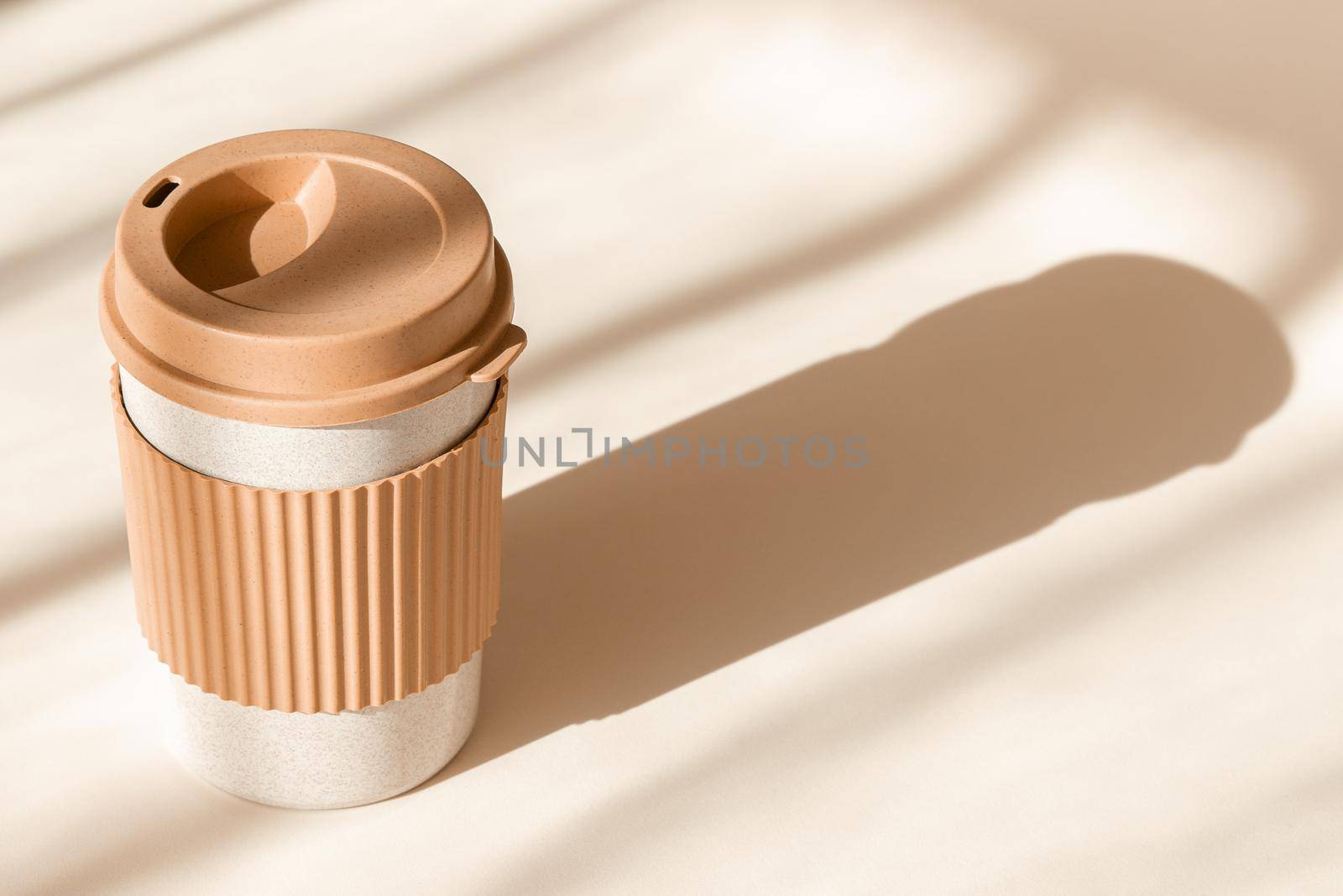 Reusable cup, biodegradable travel plastic coffee mug for take away. Sustainable bamboo eco friendly cup on natural shadow beige background. Zero waste, sustainability concept by photolime