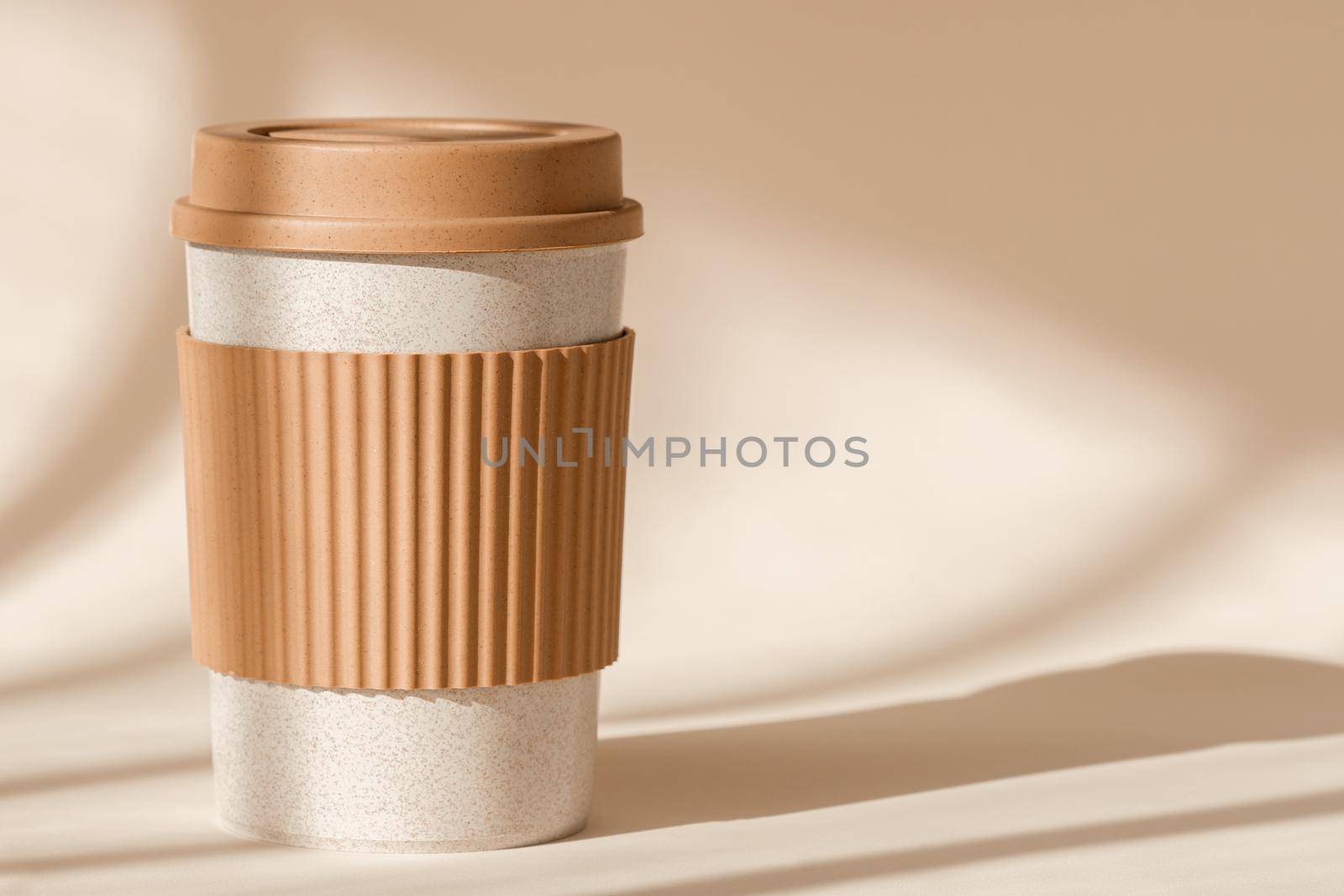 Sustainable bamboo eco friendly cup with silicone holder on natural shadow beige background. Reusable, biodegradable travel plastic coffee mug for take away. Zero waste, sustainability by photolime
