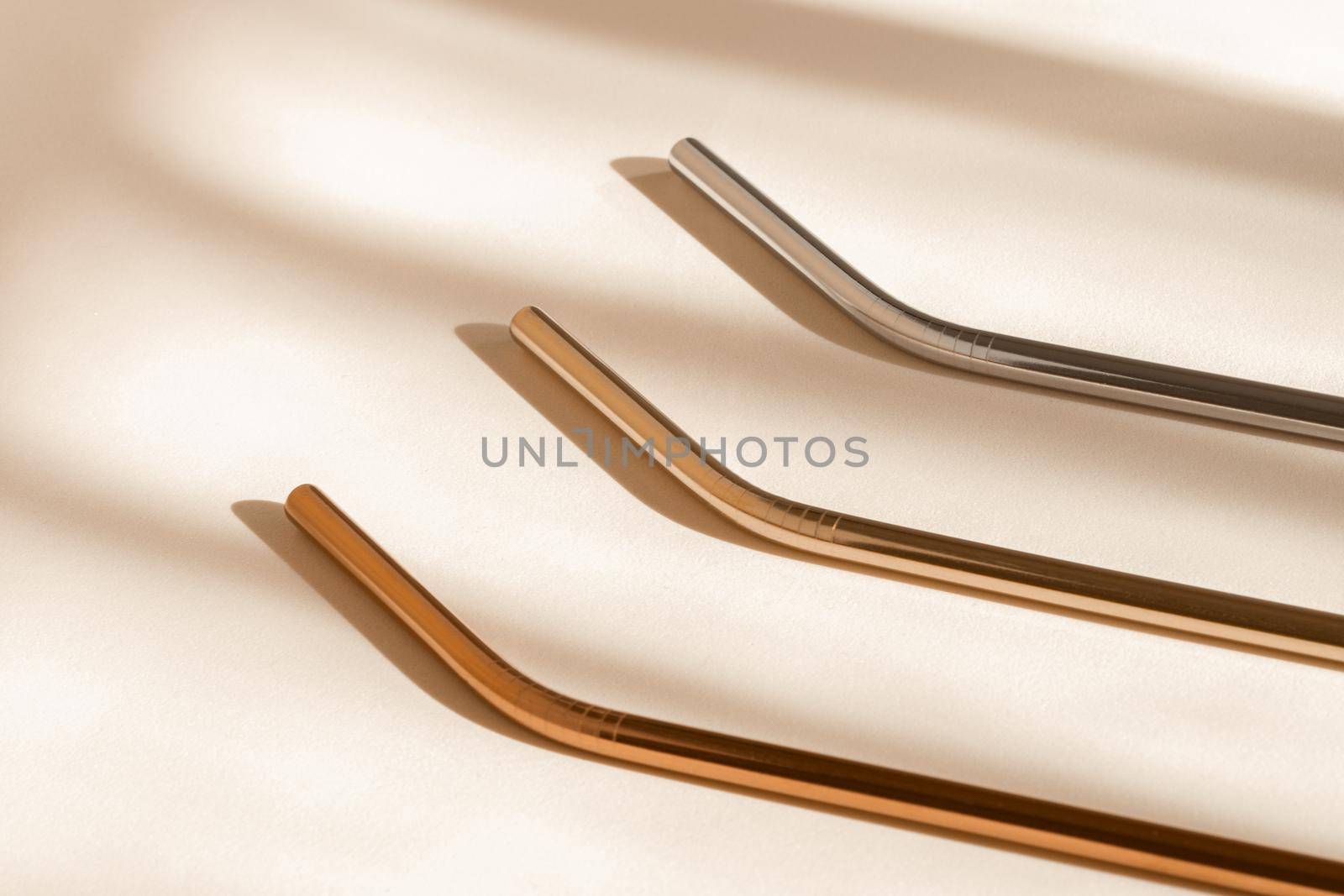 Eco friendly drinking straws from aluminium or stainless steel, reusable zero waste metal straw on neutral beige background with shadow from room windows, high angle view. by photolime