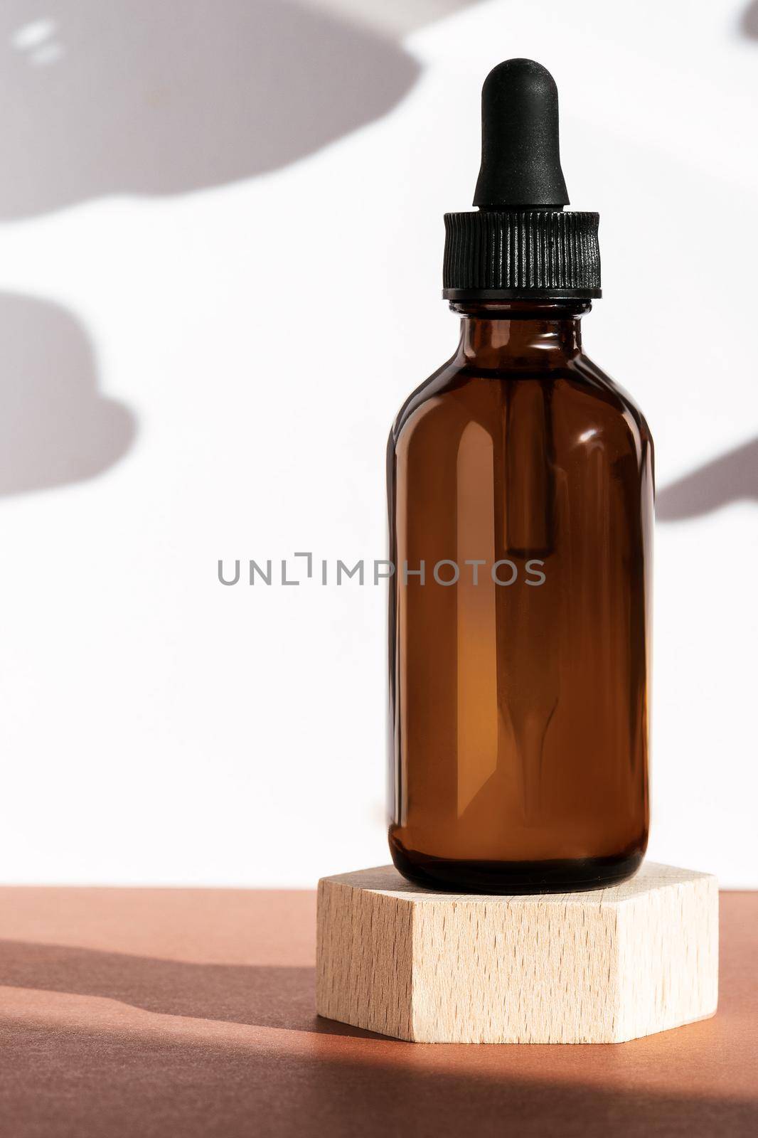 Amber cosmetic bottle on wooden geometric pedestal podium, product packaging with natural shadows from plants, anti aging serum with peptides, cosmetics mockup, biophilic concept. Front view, vertical