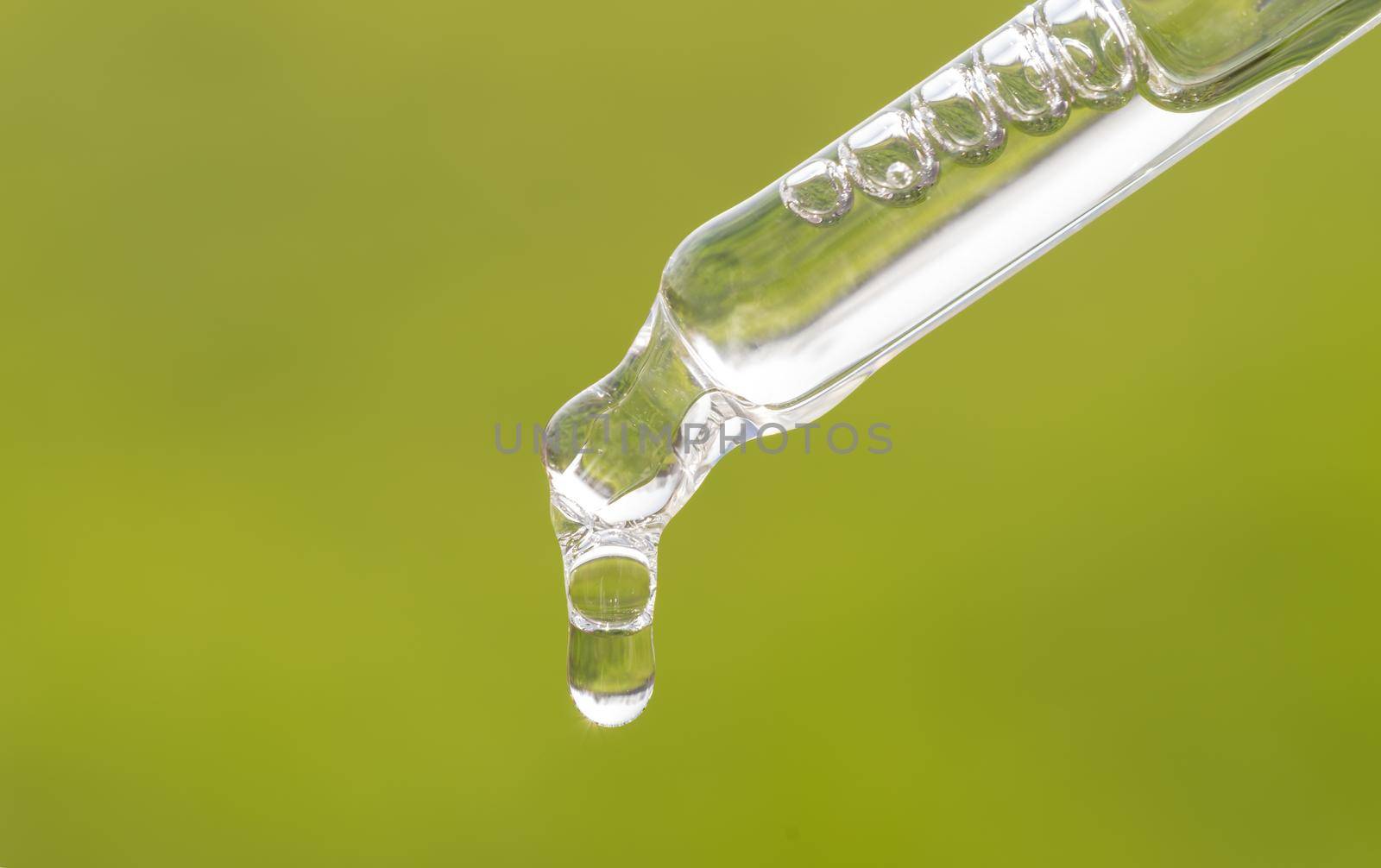 Pipette with essential oil, serum, hyaluronic acid on grass background. Aromatherapy, alternative medicine with green leaf. Closeup of green pippette, falling drop. Beauty skin care product by photolime