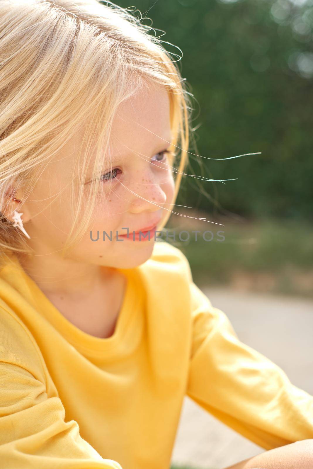 Pretty beautiful blonde child girl sitting before green wall. Smiling preschool girl 5 - 6 years old in yellow t shirt looking at camera. Lifestyle. Beauty. Summer vacation. Leisure. People