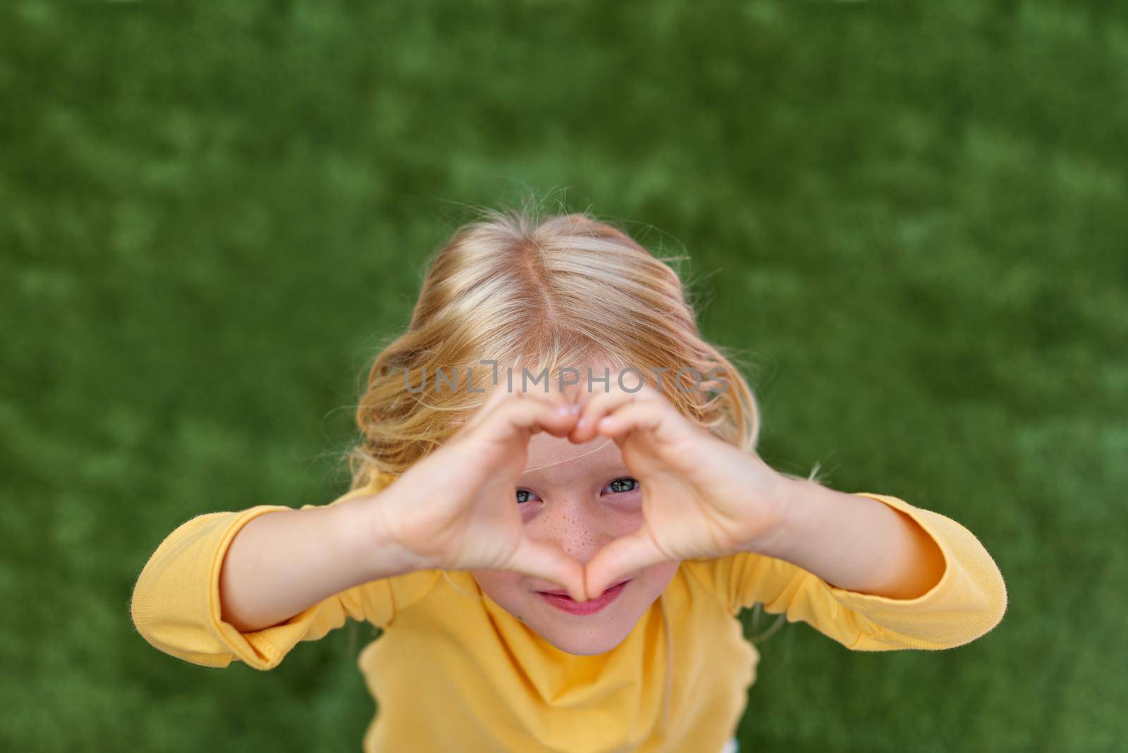 Pretty blonde child girl showing sign of love heart from fingers hands. Top view by OlgaPink