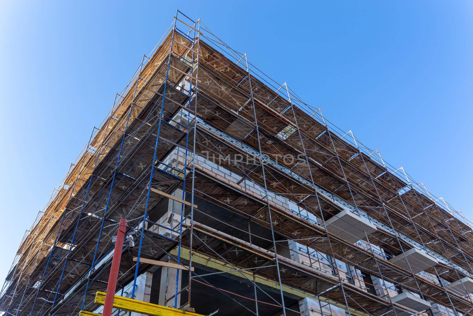 Insulation of the exterior walls of a building under construction. The walls of the building under construction are surrounded by scaffolding for workers to access. Exterior finishing works.