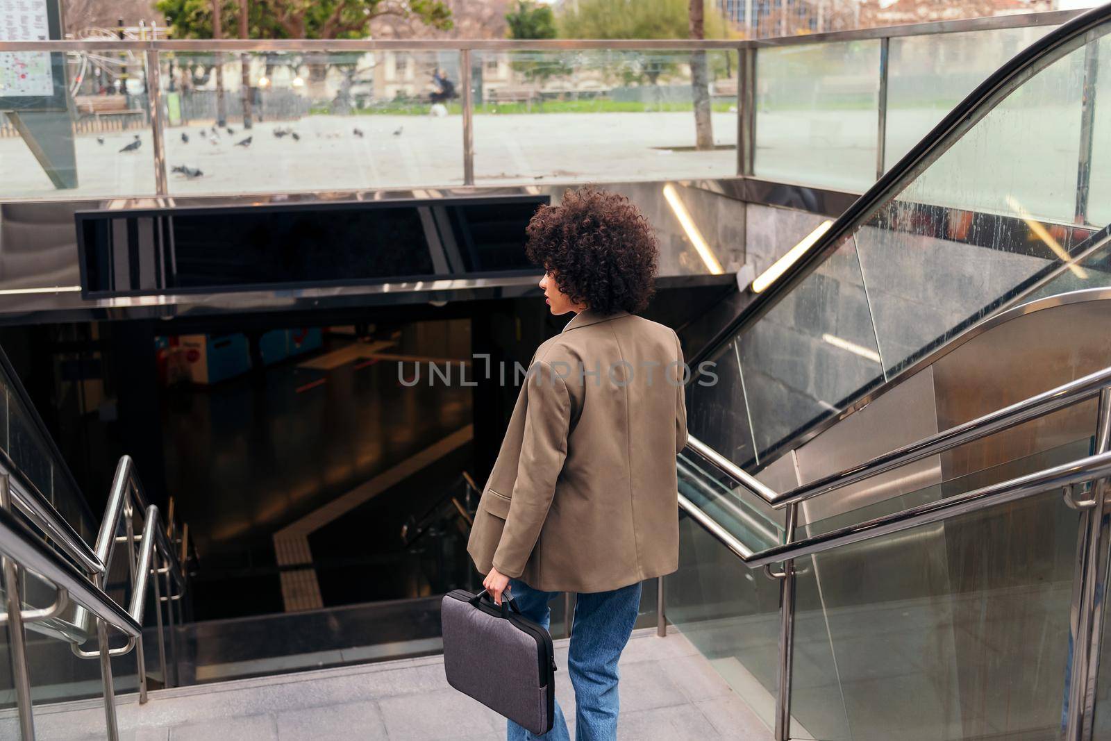 rear view of a successful business woman entering to the subway station with her briefcase, concept of urban lifestyle and public transport, copy space for text