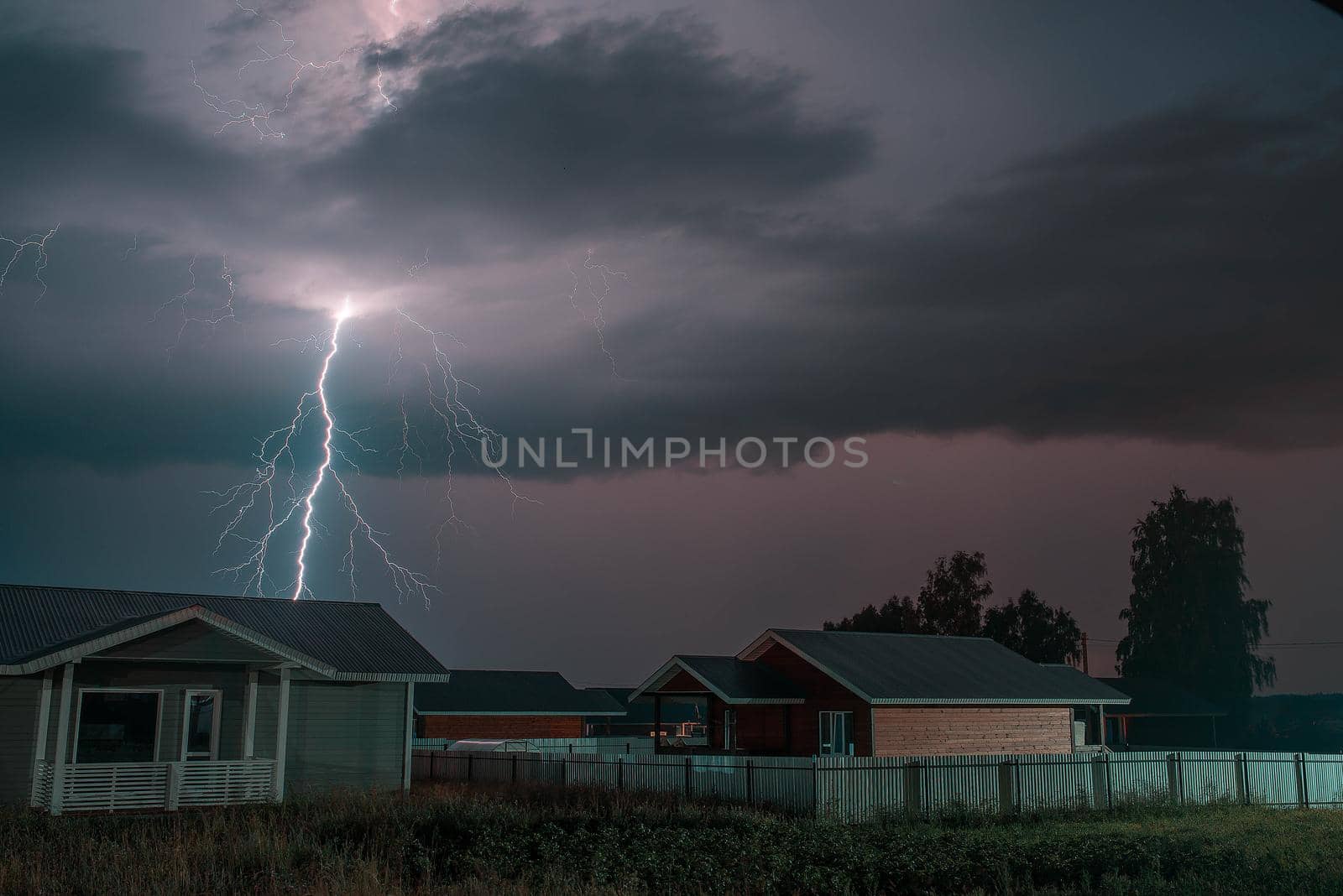 Thunderbolt over the house in the village and dark stormy sky on the background by Hitachin