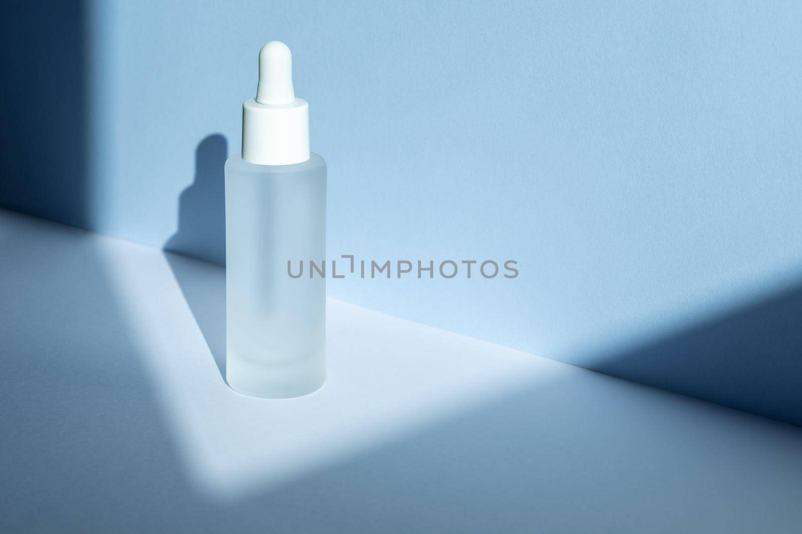 Glass cosmetic bottle with pipette product packaging with geometric shadows on blue background, anti aging serum with collagen and peptides, cosmetics mockup, skincare concept. High angle view