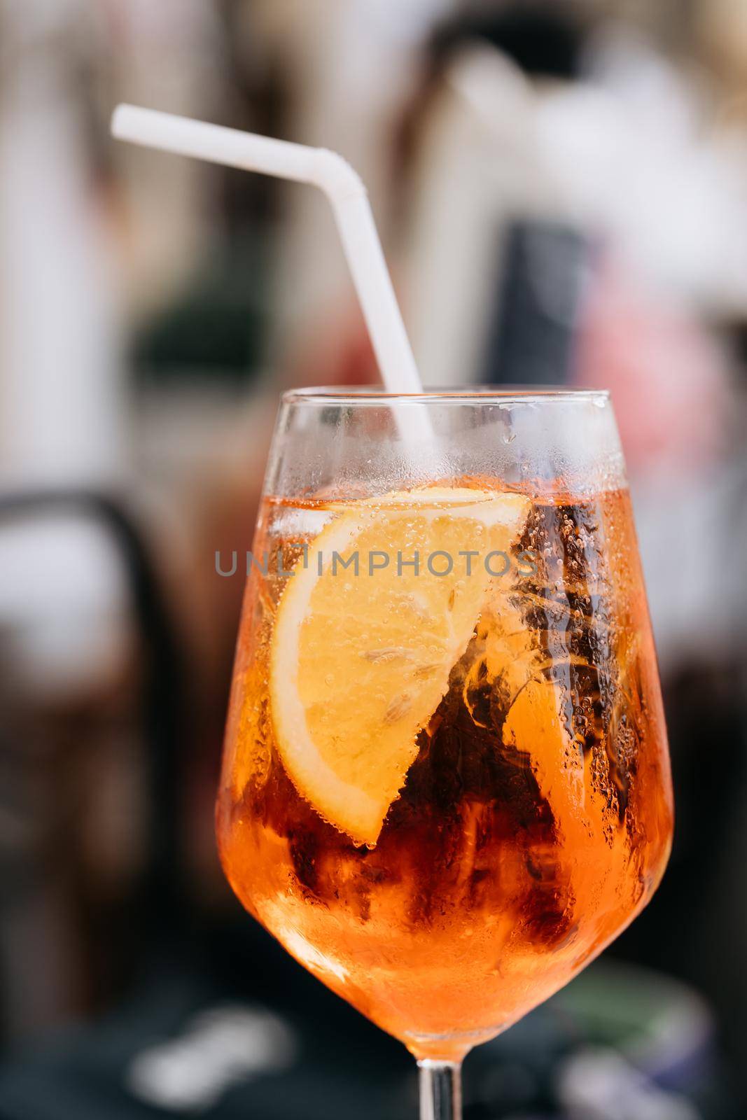 Glass of ice cold Aperol spritz cocktail served in a wine glass, decorated with slices of orange with straw. Aperitive in street caffe in Italy